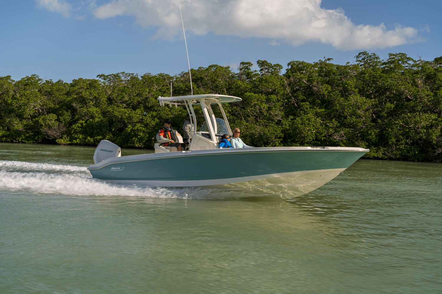 A Boston Whaler 25DA boat speeds through calm water, surrounded by lush greenery.