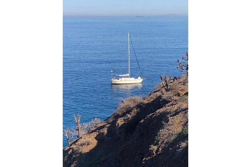 Sailboat Caliber 33 (1991) anchored in calm blue ocean near rocky coastline.