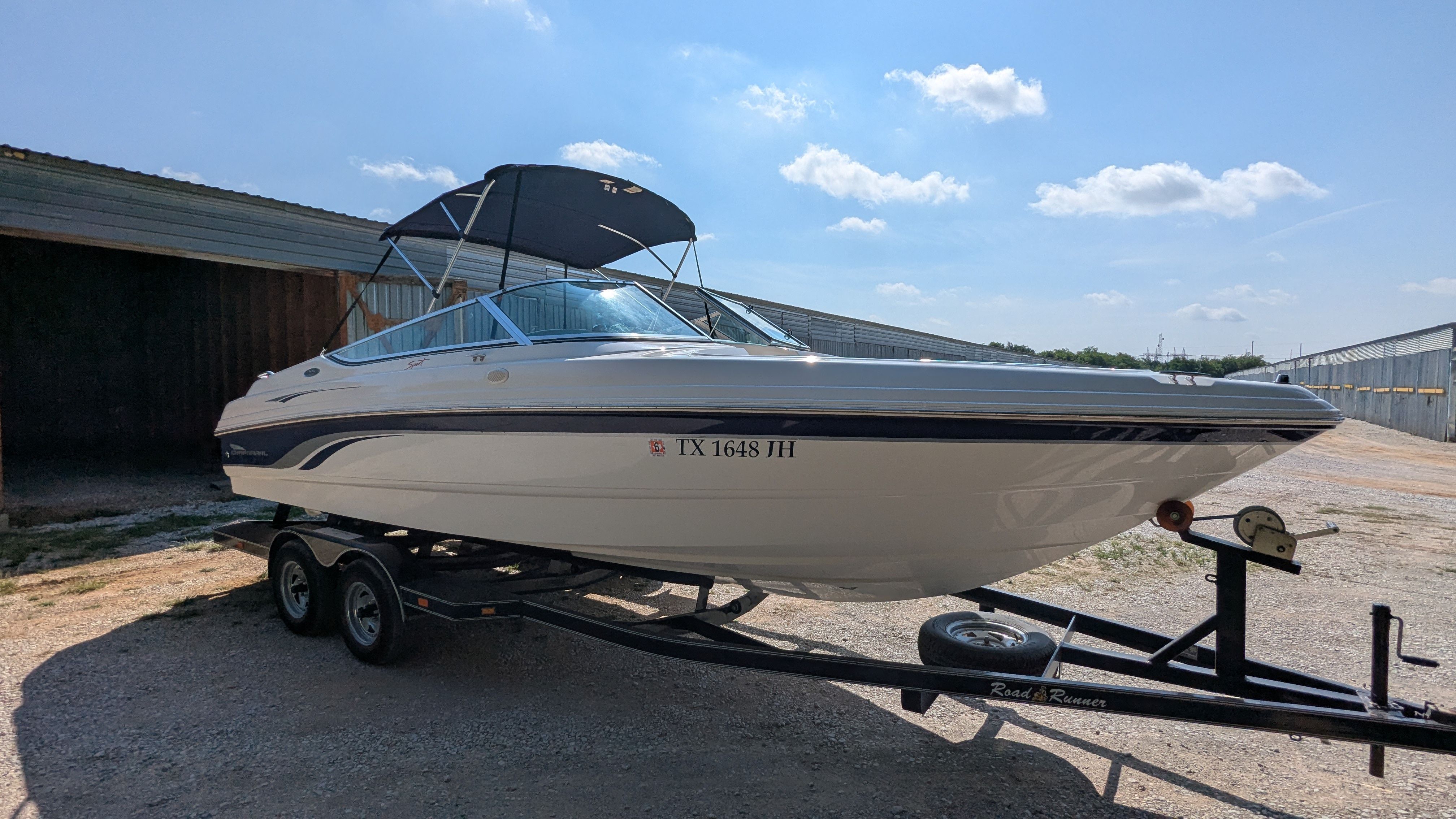 2000 Chaparral 240 SSi on a trailer, with a blue bimini top, in front of a building.