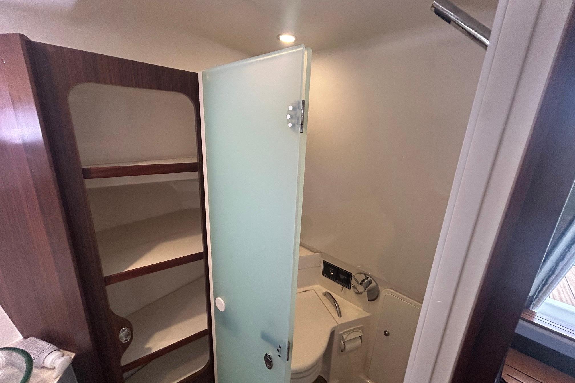 2019 Pursuit OS 355 Offshore bathroom with frosted glass door and wooden shelving.