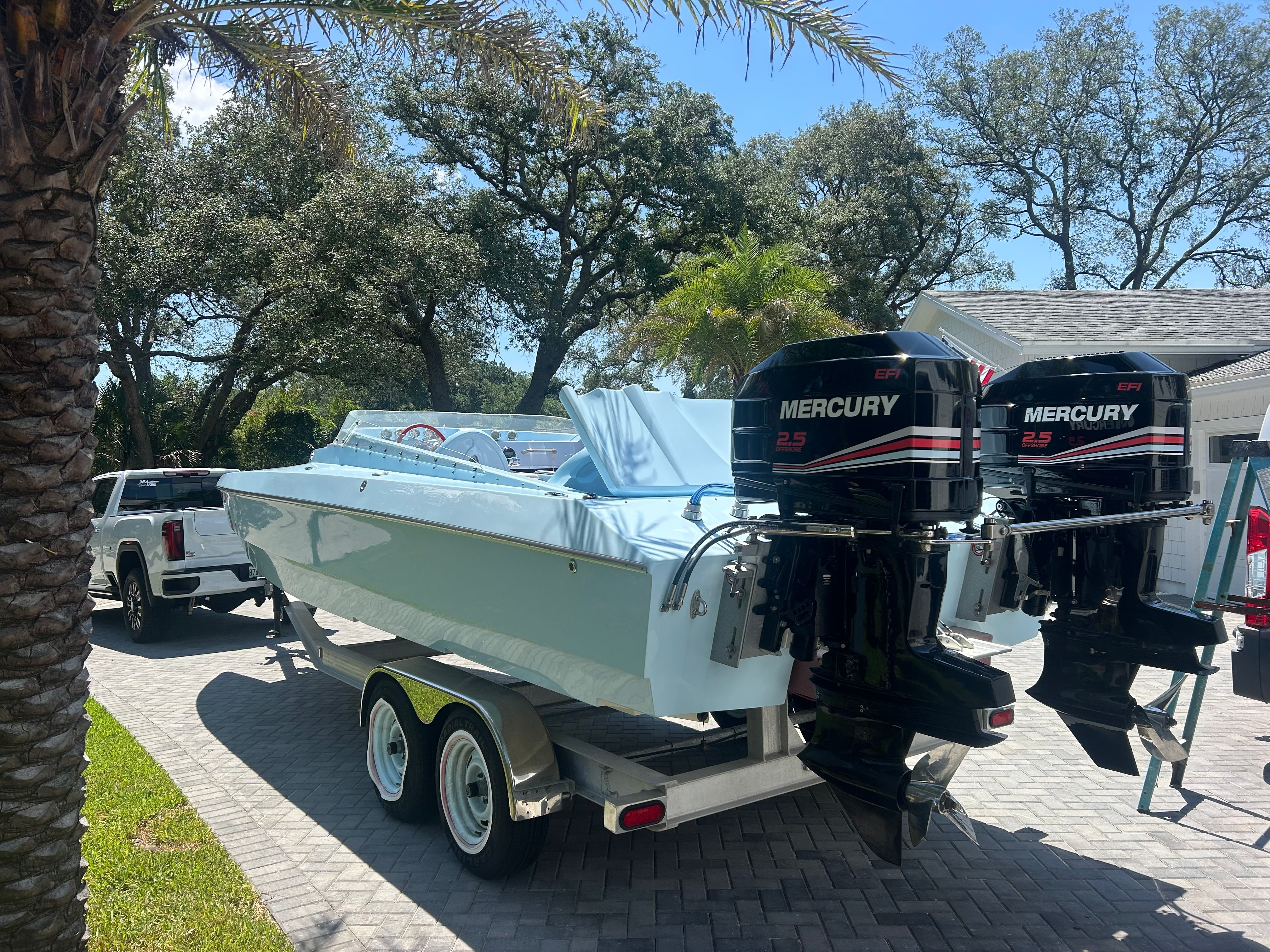 A 1992 Motion Marine 25 CAT boat on a trailer with two Mercury engines, surrounded by trees.