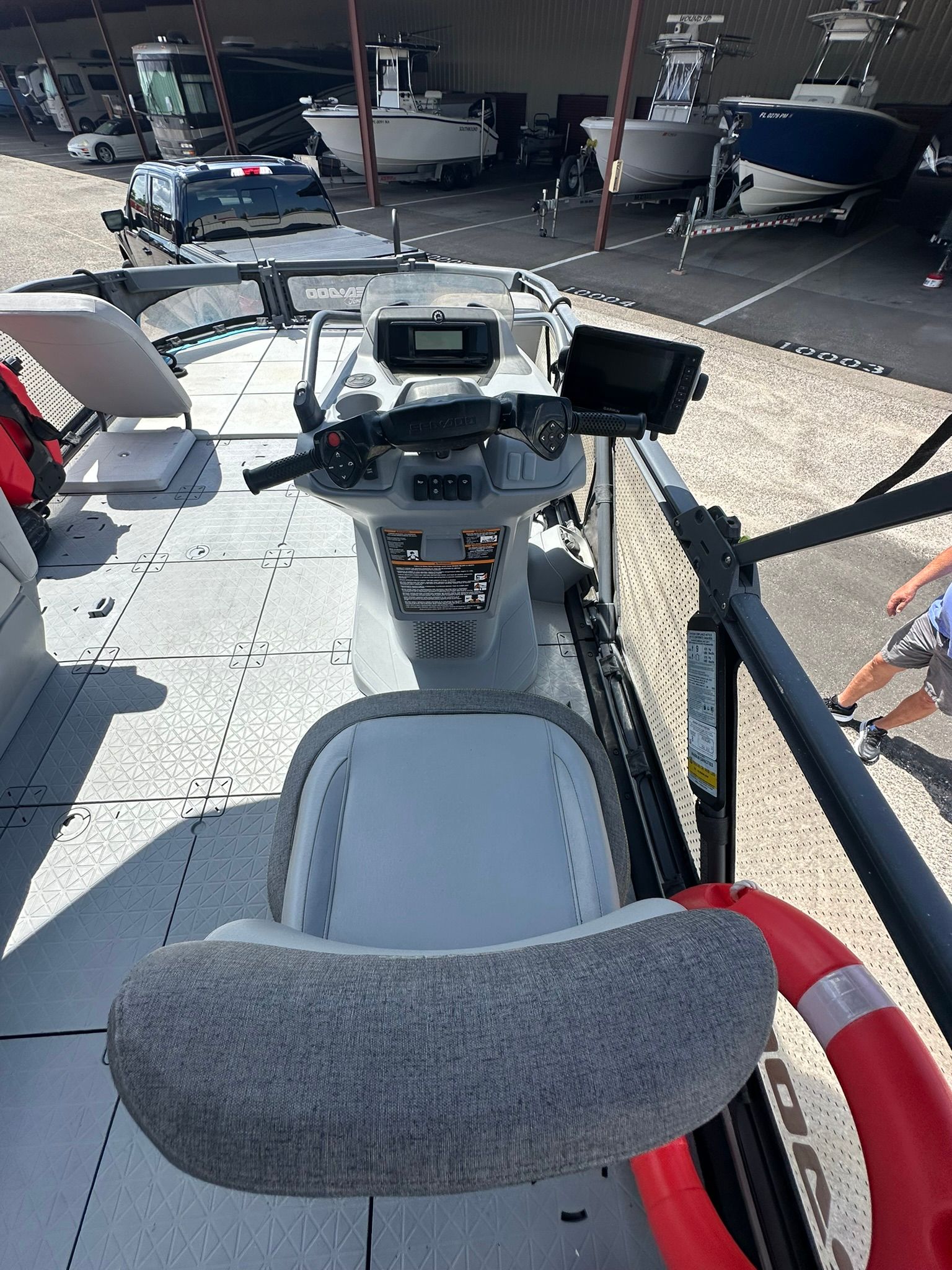 The image shows the cockpit of a 2023 Sea-Doo 21 SWITCH SPORT. It features a modern helm with a screen and a gray seat. Other boats are visible in a storage area in the background.