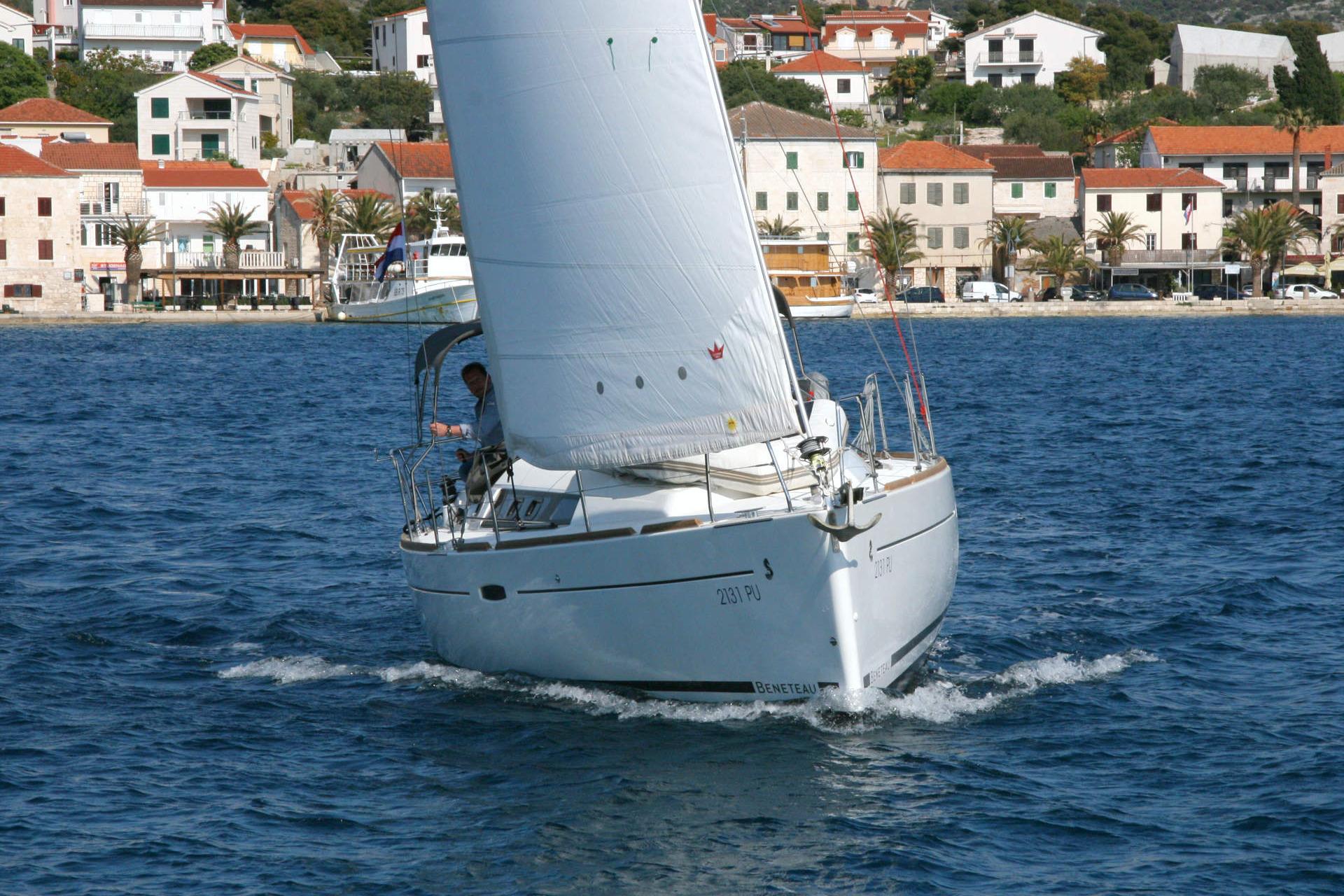 2014 Beneteau Oceanis 34 sailing near coastal town with red-roofed buildings.