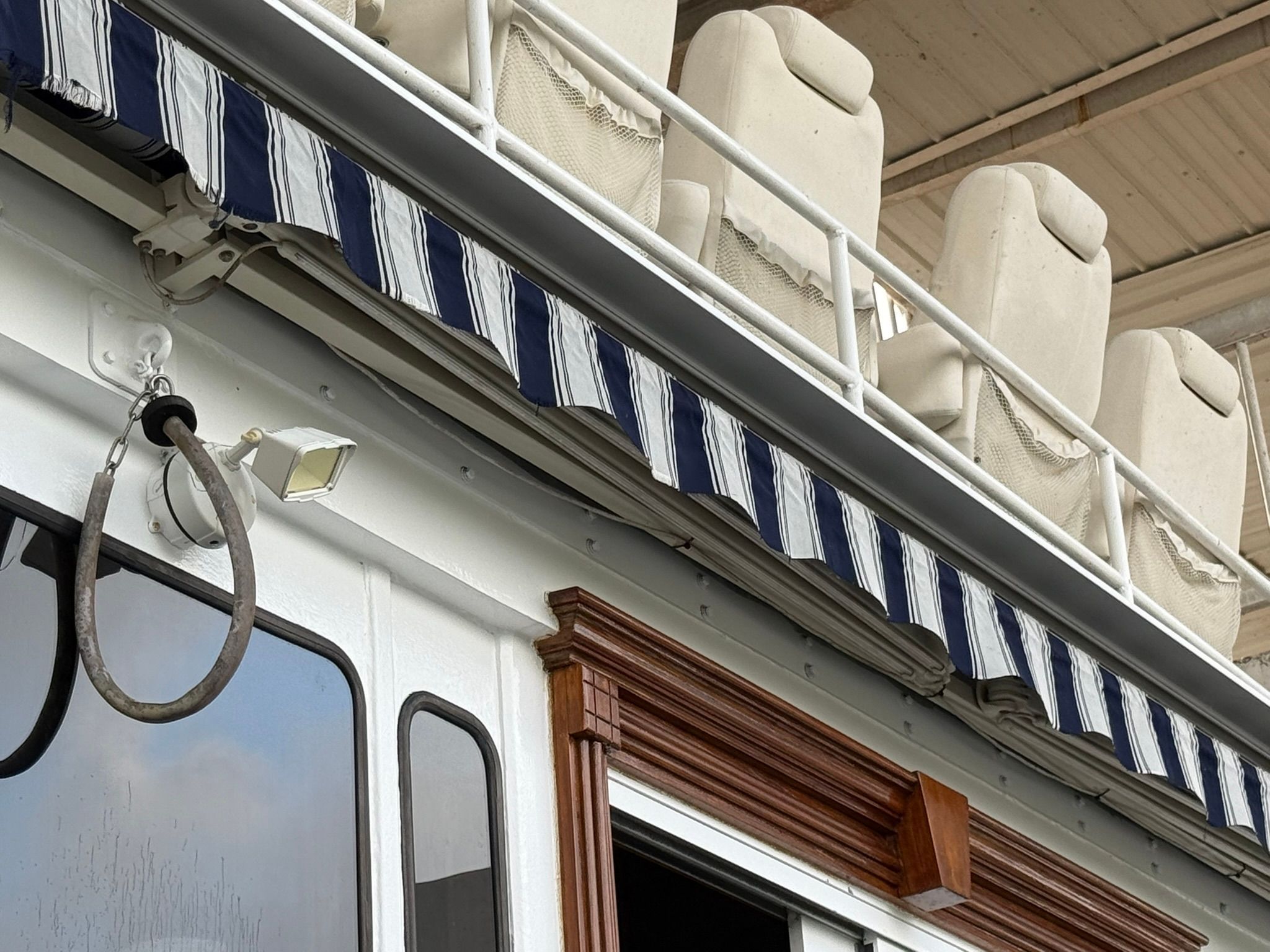 A boat with a striped awning and white seats on the upper deck.