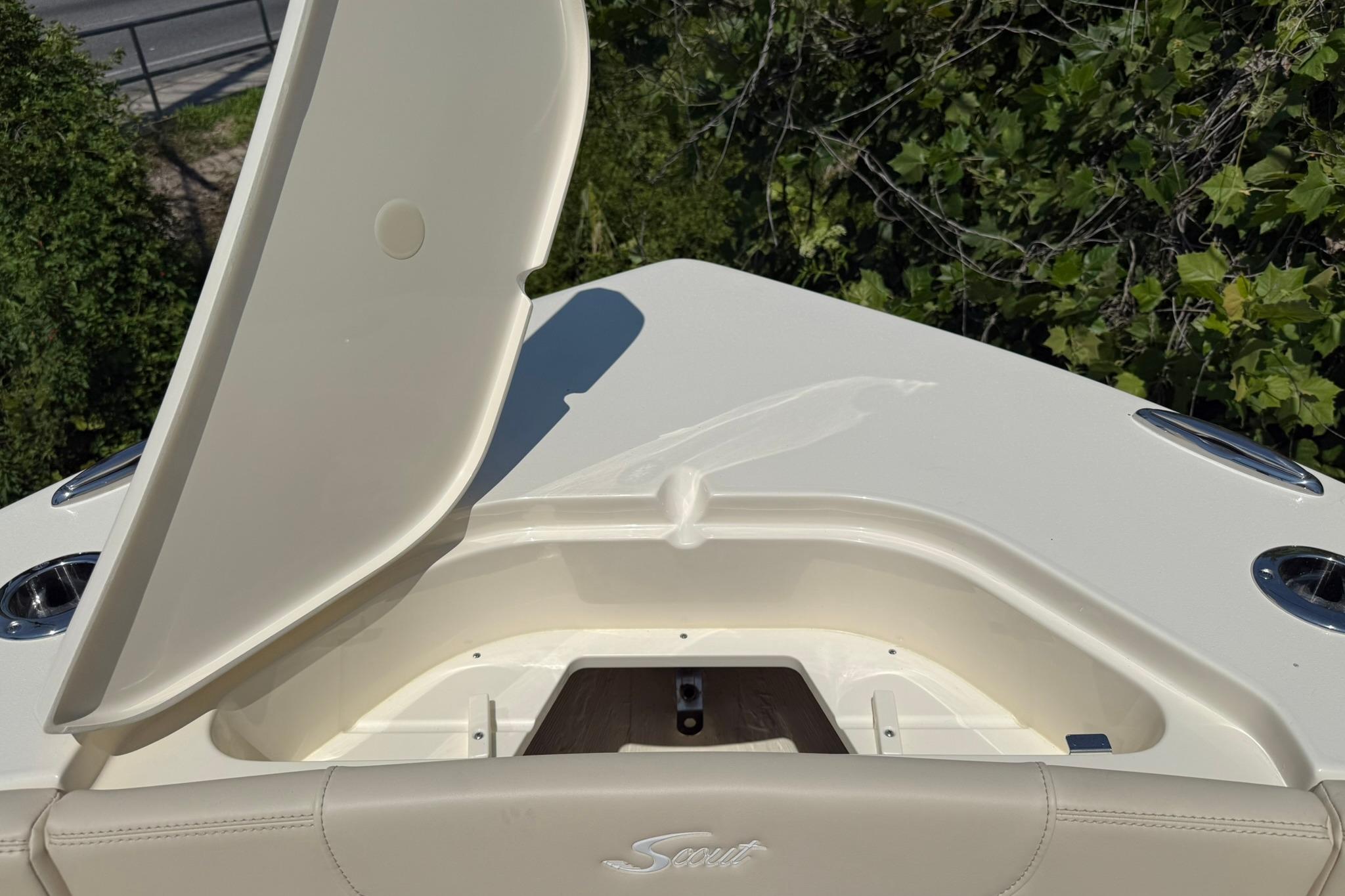 2027 Scout 240 XSF boat with open storage compartment, surrounded by greenery.