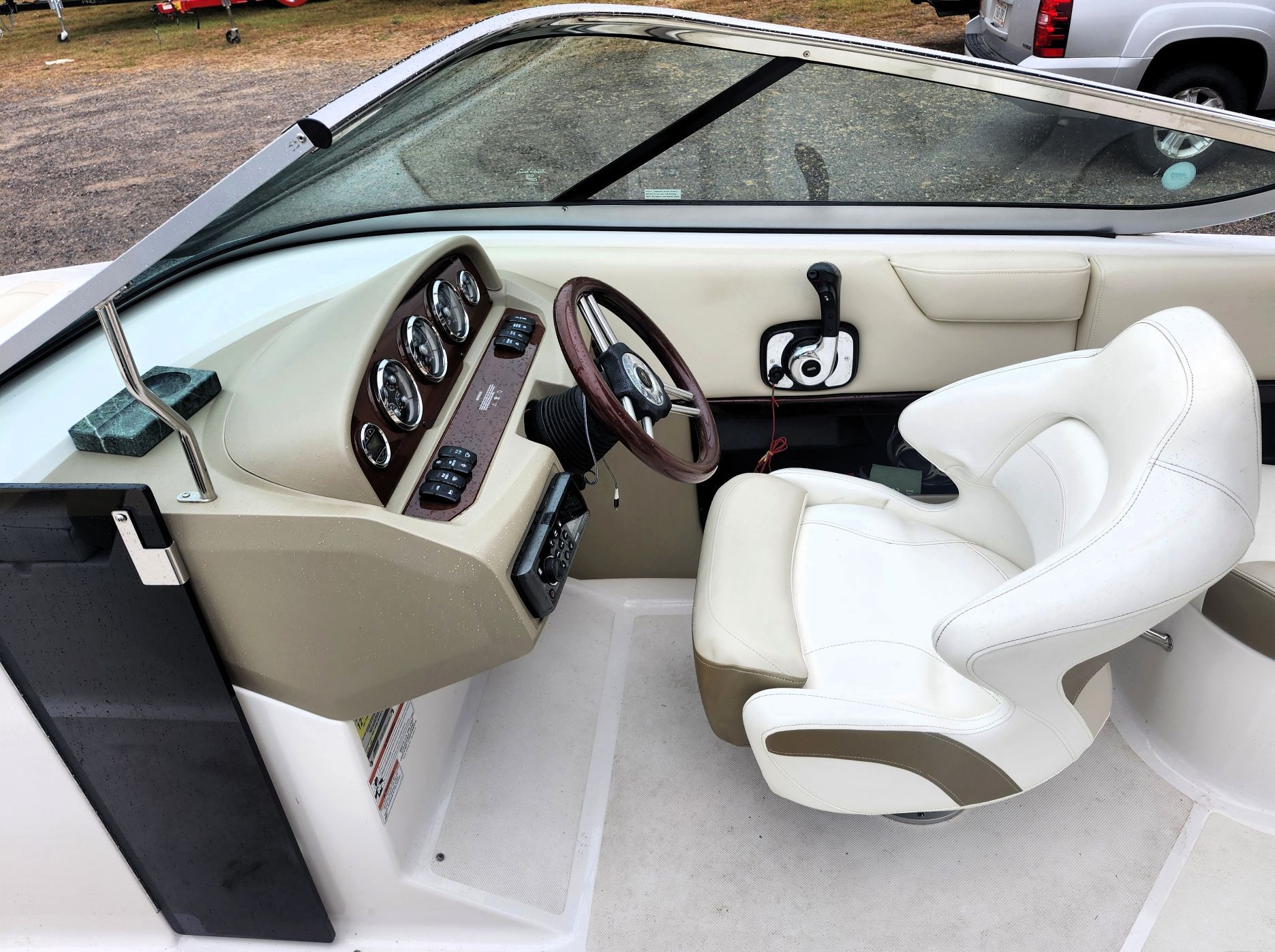 The image shows a boat's cockpit with a white seat and a wooden steering wheel.