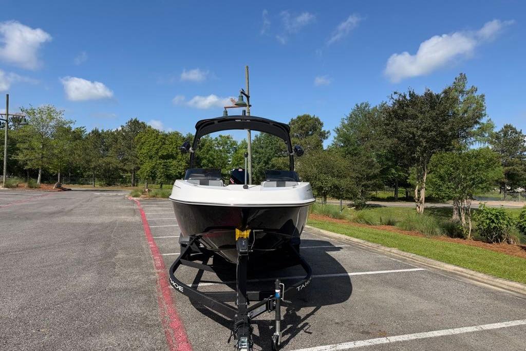 2026 Tahoe T21 boat on trailer in parking lot, surrounded by trees and blue sky.