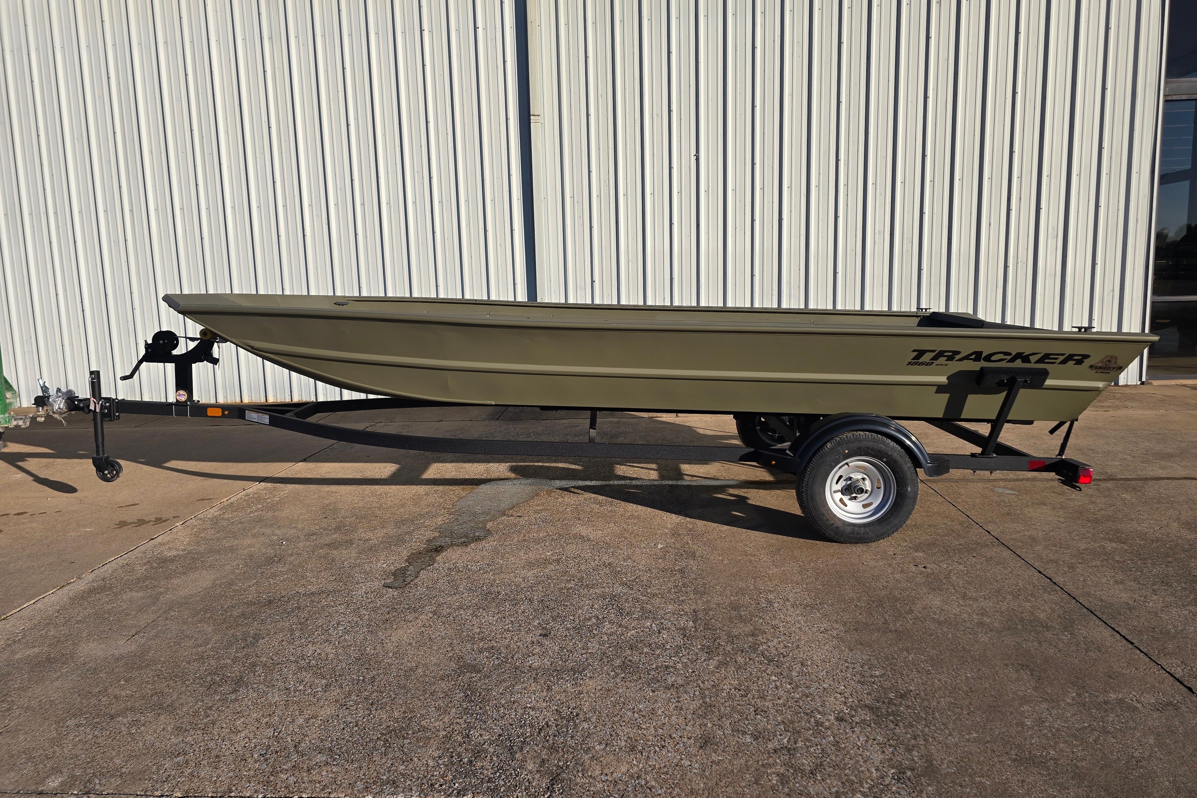 2025 Tracker Grizzly 1860 Utility boat on trailer, parked outside a metal building.