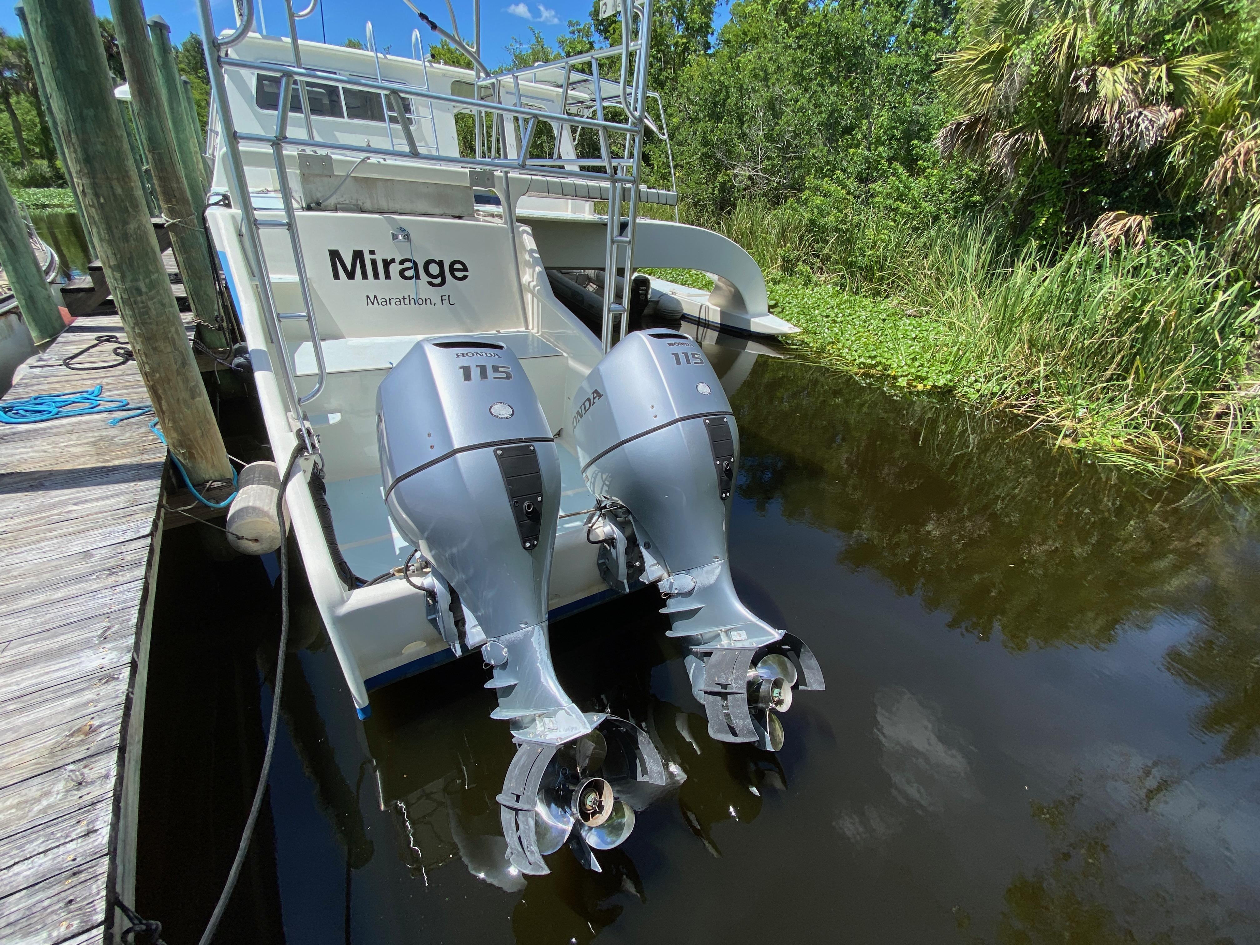 Boat with twin Honda 115 outboard motors docked near lush greenery.