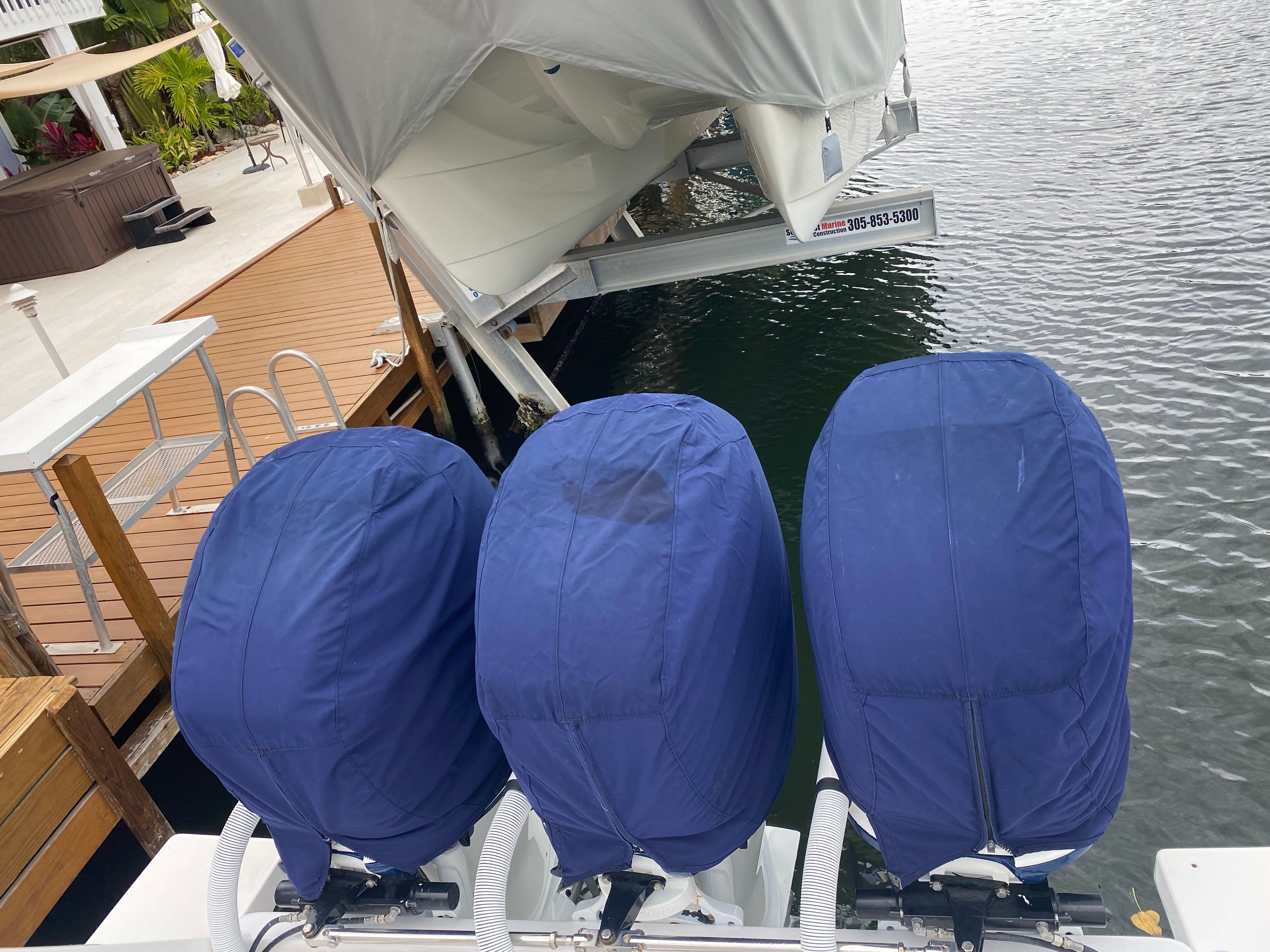 Three outboard motors with blue covers on a boat docked by a wooden pier.