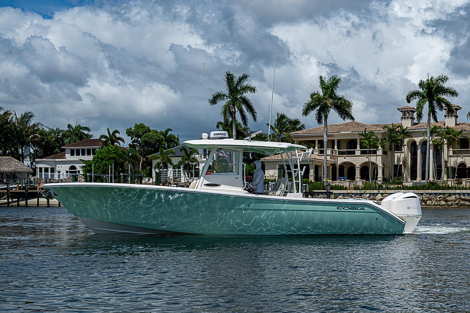2019 Cobia 320 Center Console boat cruising near luxury waterfront homes.
