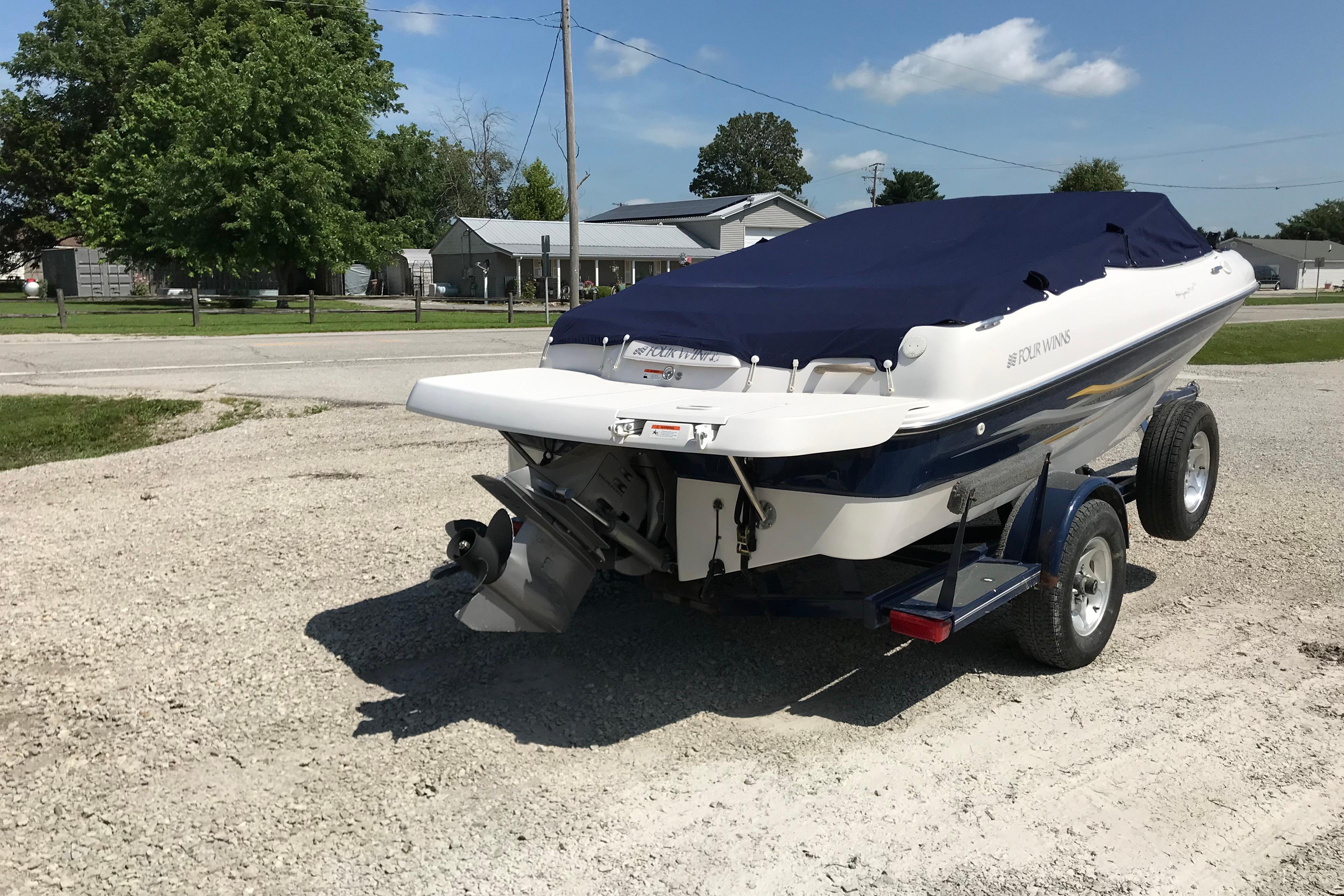 2005 Four Winns 180 Horizon FS boat on trailer, covered, parked on gravel.