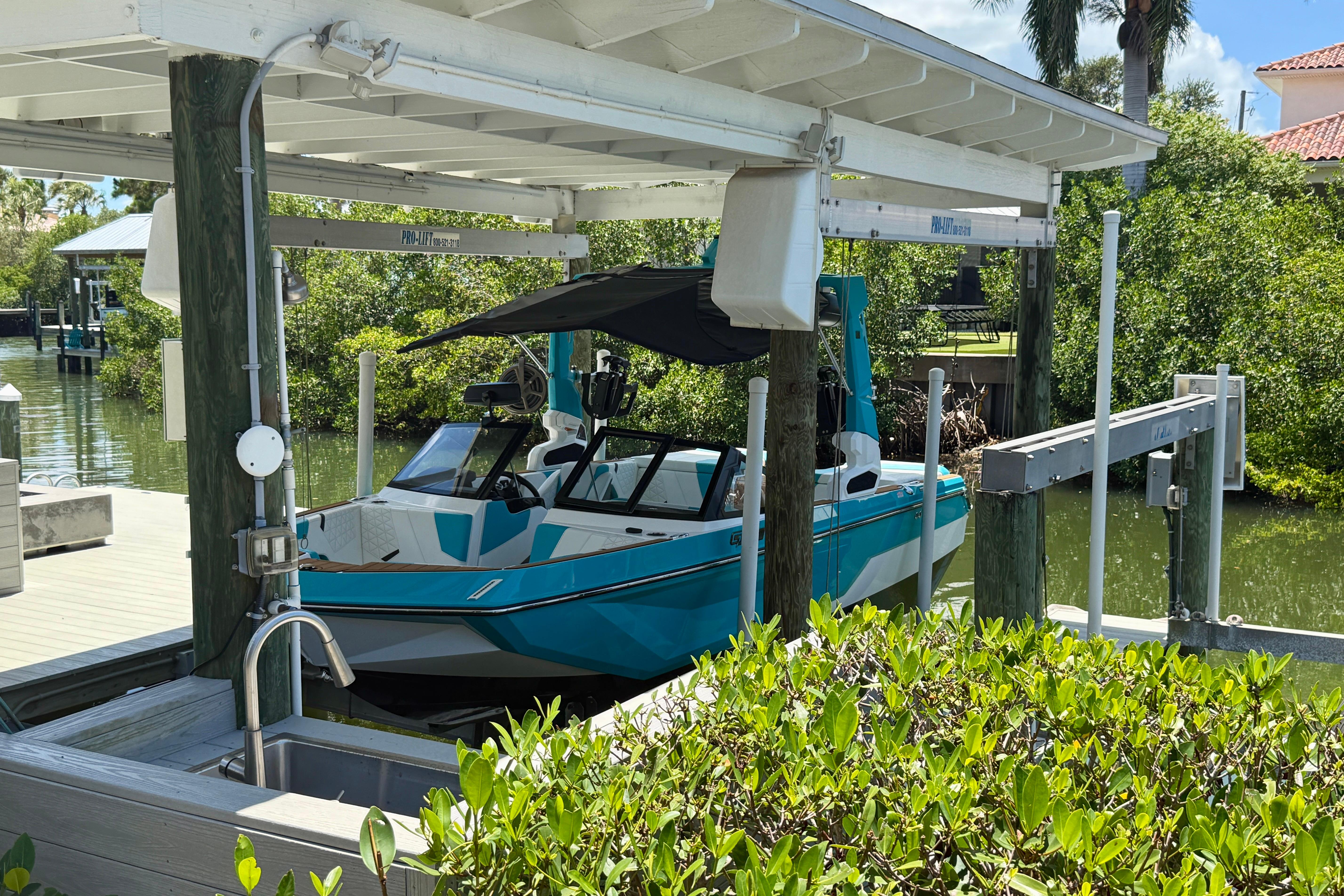 2024 Nautique Super Air Nautique GS20 boat docked under a covered lift in a scenic marina.