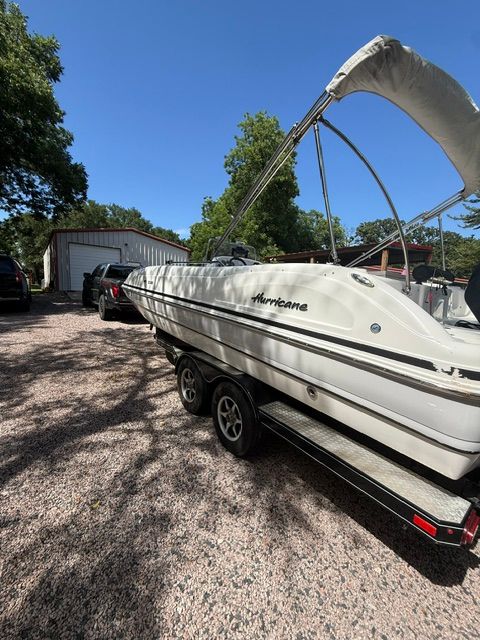 A 2016 Hurricane SunDeck Sport 231 OB boat on a trailer in a yard.