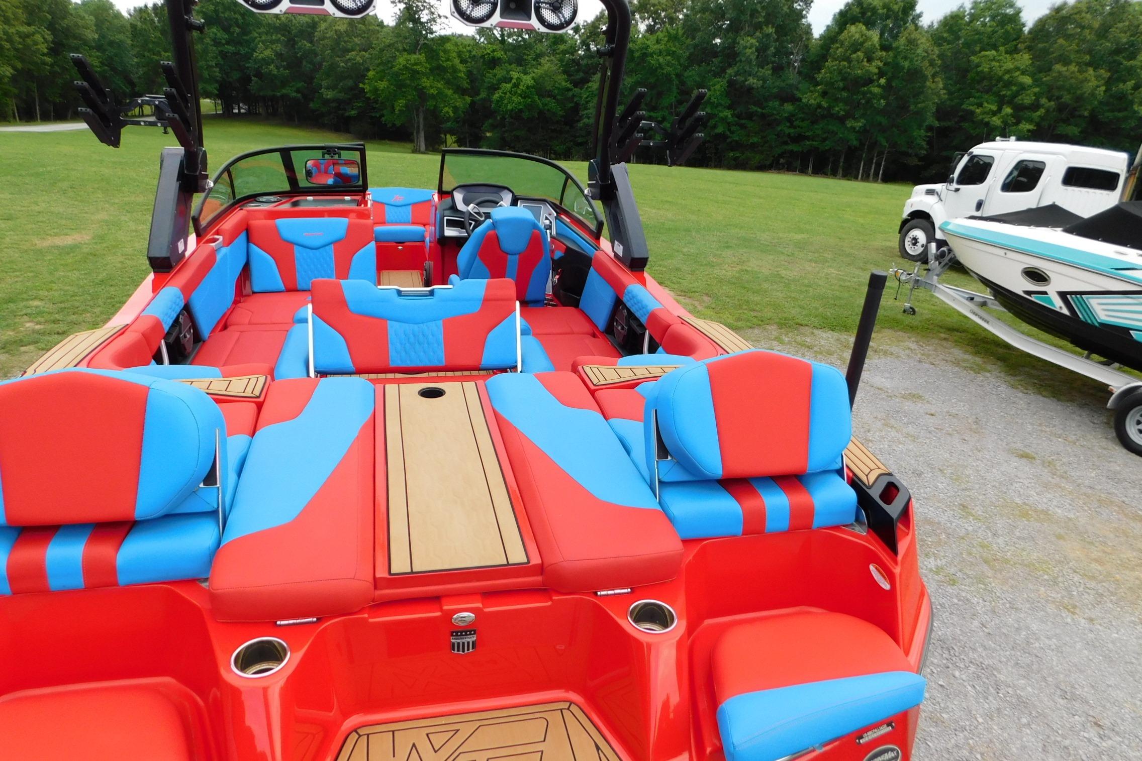 2022 MasterCraft NXT24 boat with vibrant red and blue interior, parked on grass.