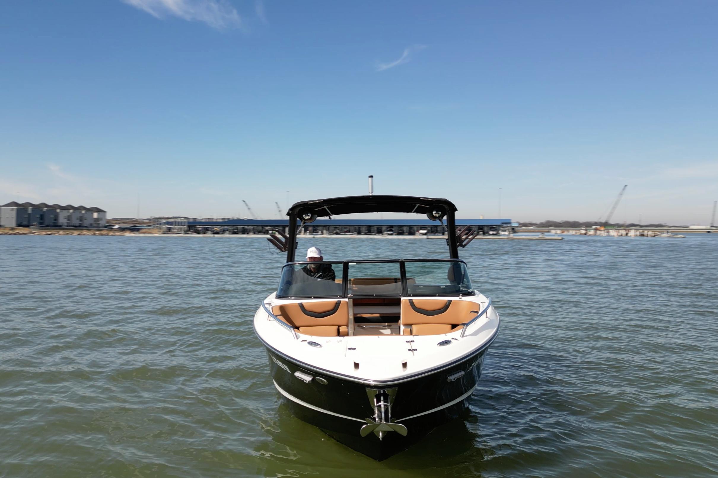 2023 Chaparral 26 Surf boat on water, clear sky, marina background.