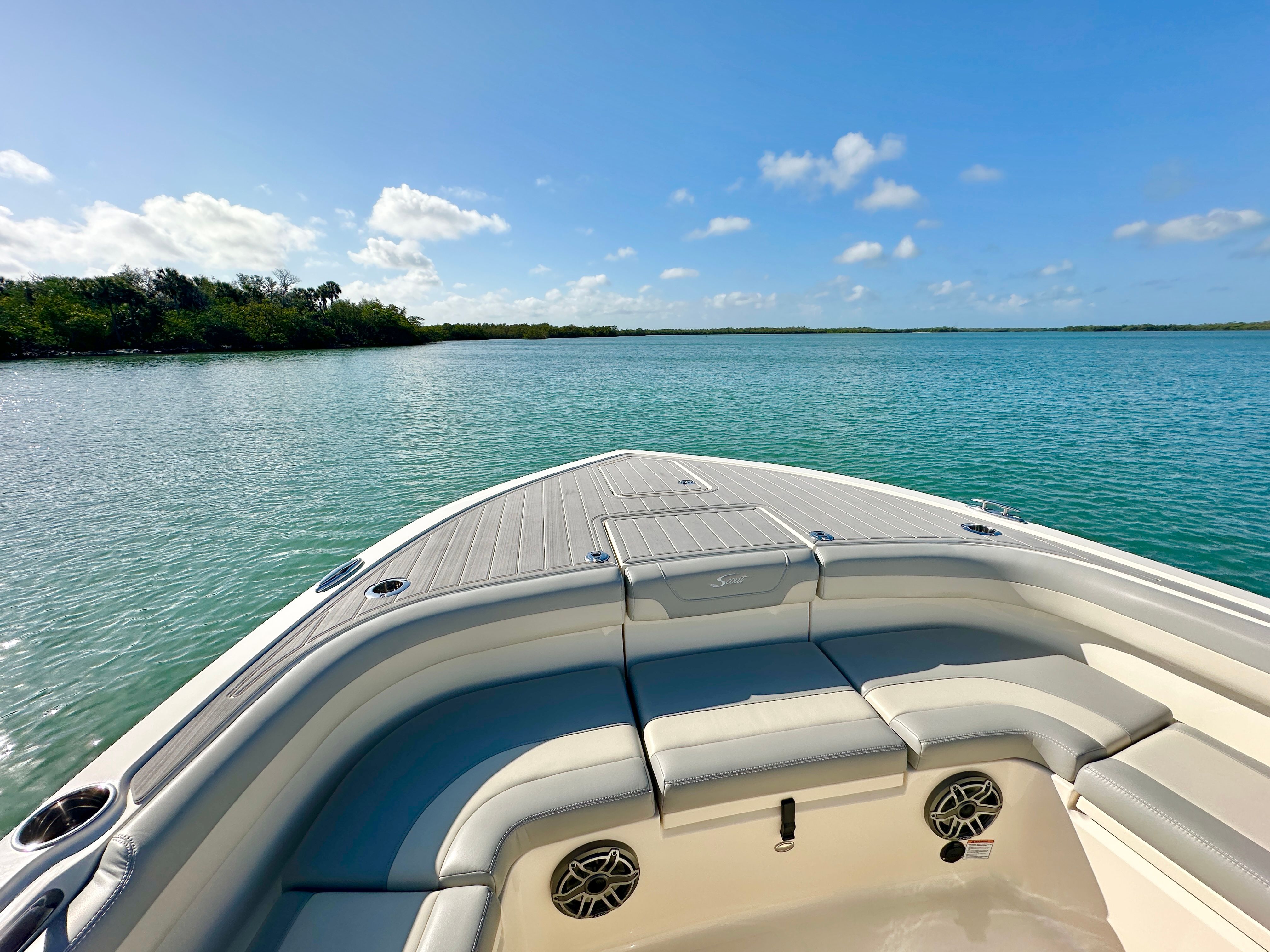 A Scout 281 XSS boat on calm water with blue sky and green shoreline.