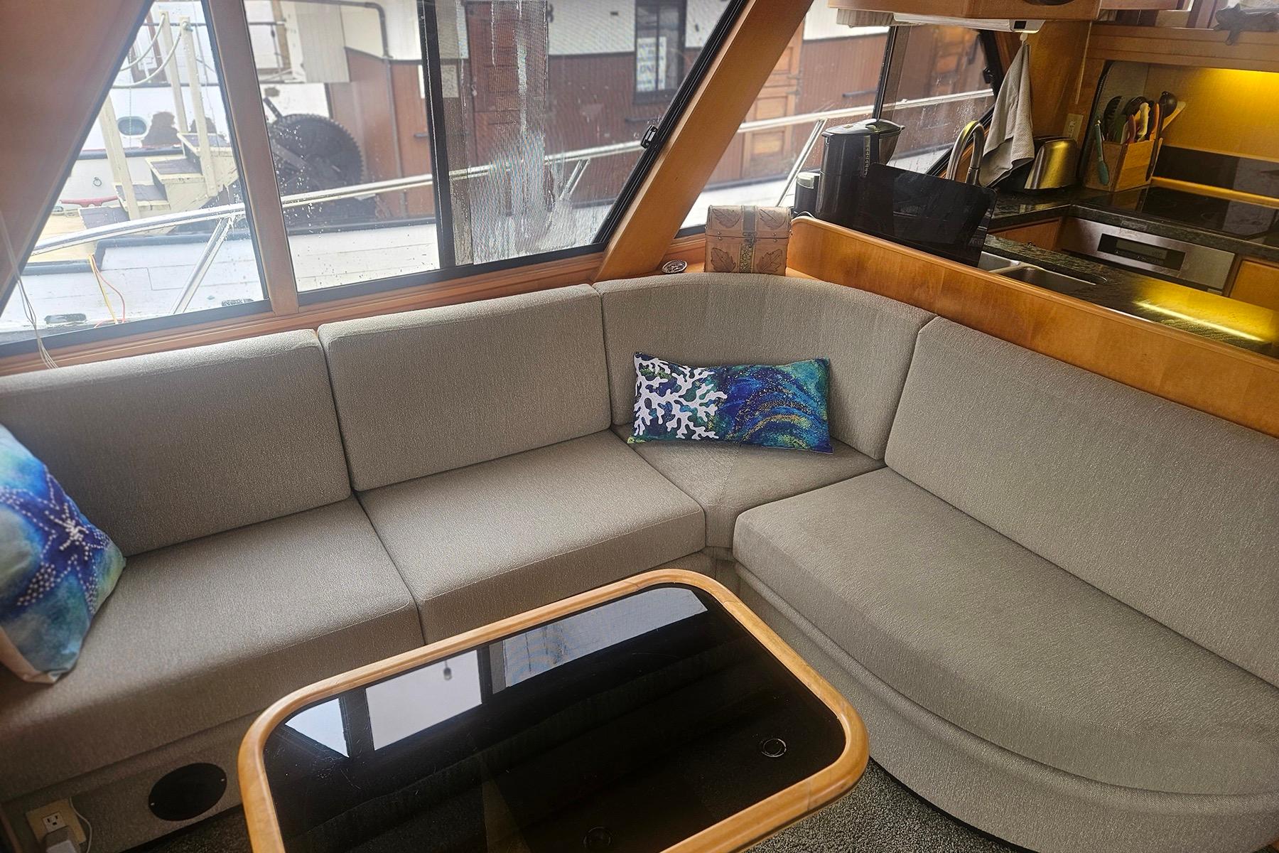 Cozy yacht interior with gray sectional sofa, colorful pillows, and wooden accents, Symbol 55, 1995.