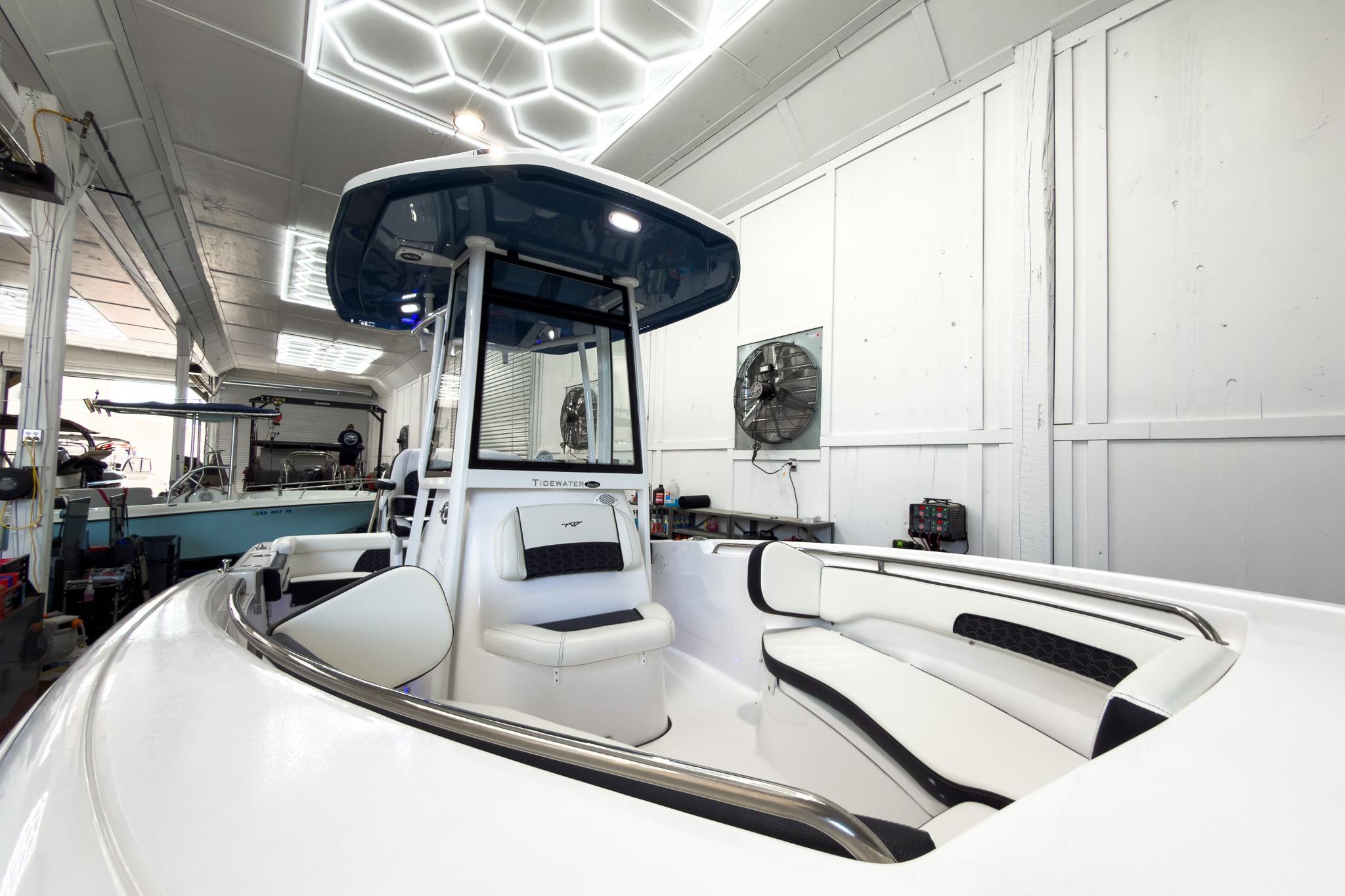The image shows a modern boat with white upholstery and a blue canopy in a showroom.