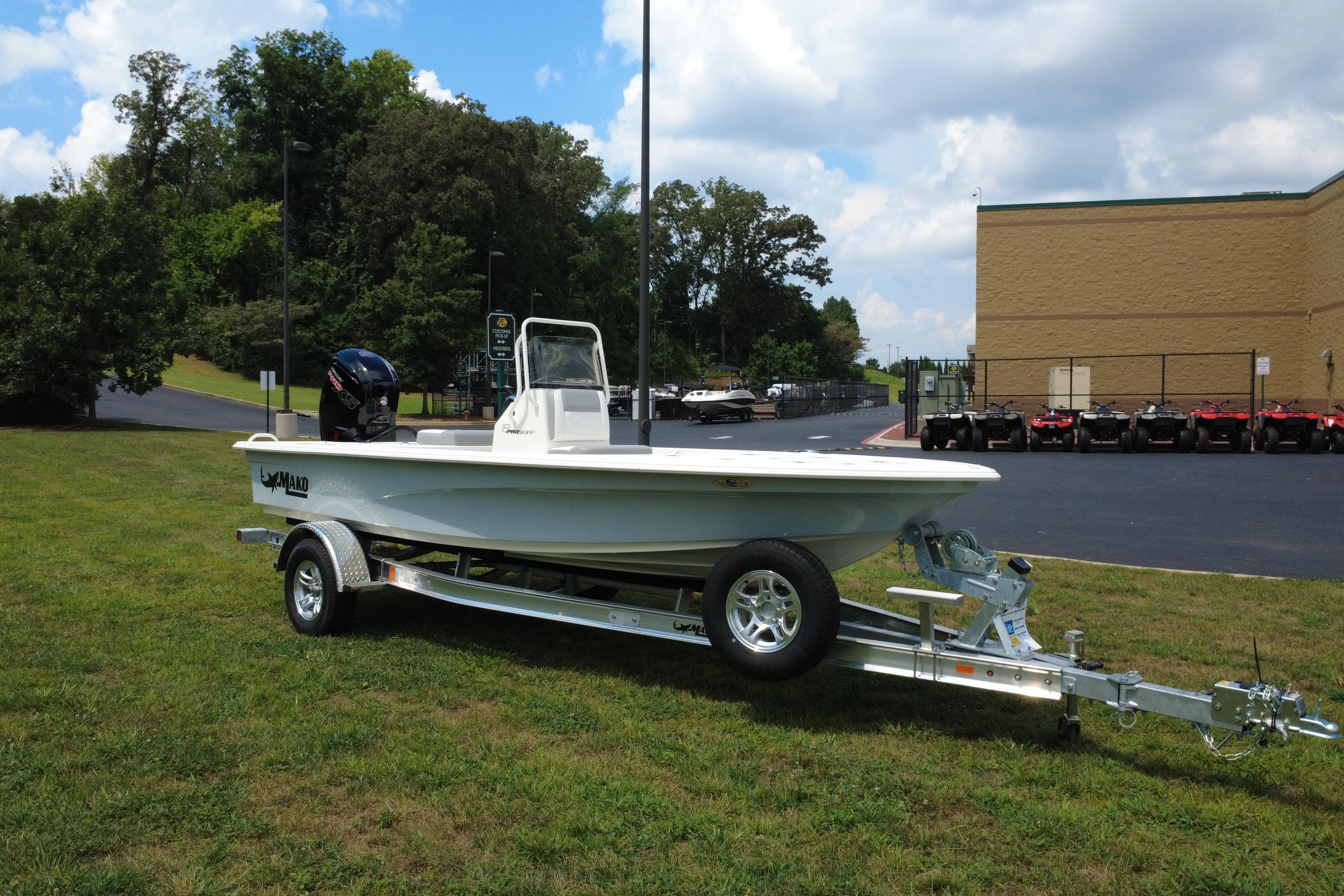 2026 Mako 18 Pro Skiff boat on trailer, parked on grass under a cloudy sky.