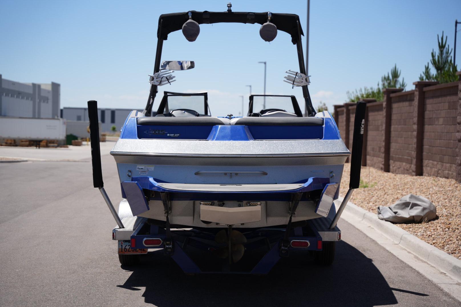 2015 Axis A24 boat, blue and silver, parked on a street near a brick wall.