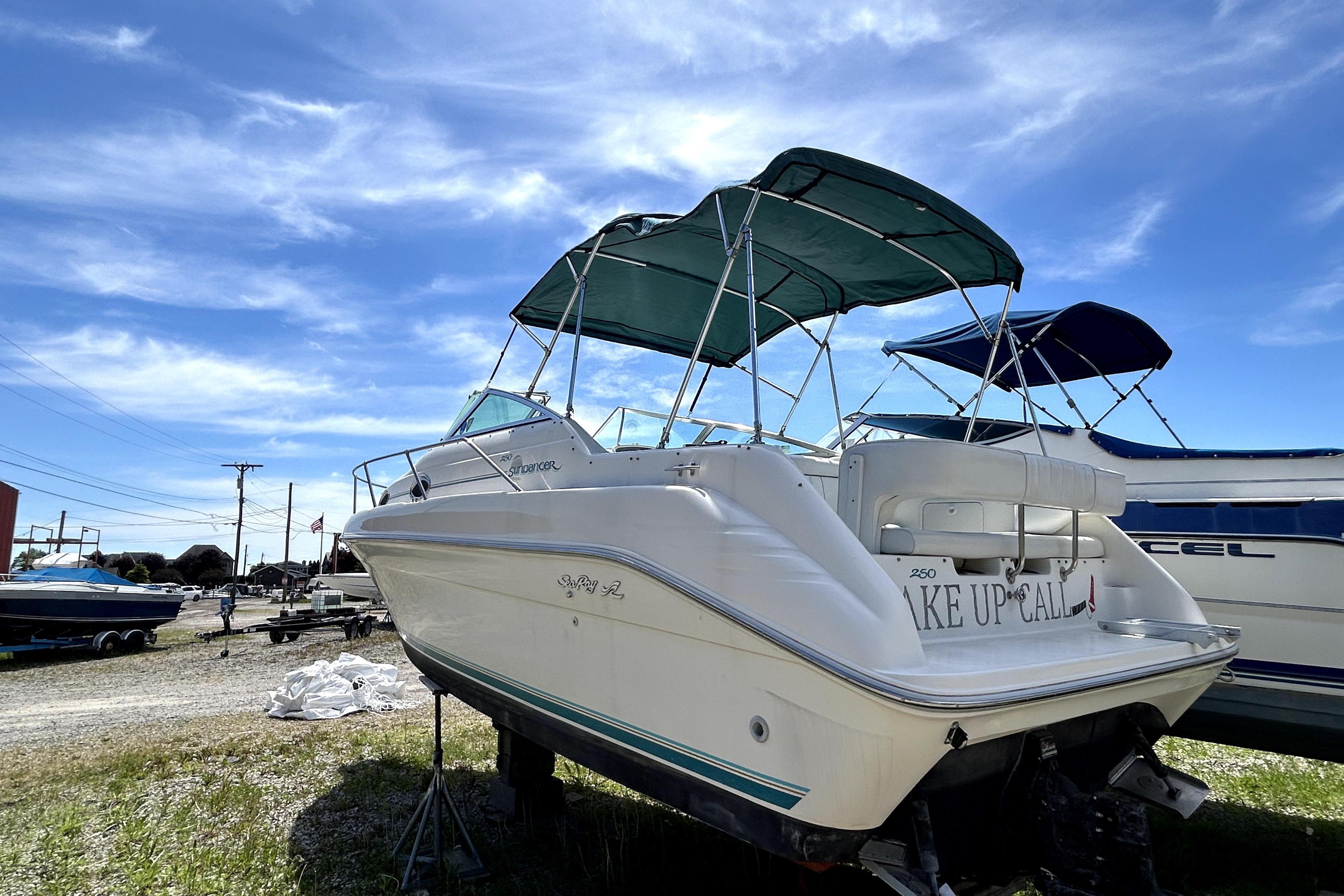1995 Sea Ray 250 Sundancer boat with green canopy, parked outdoors under a blue sky.