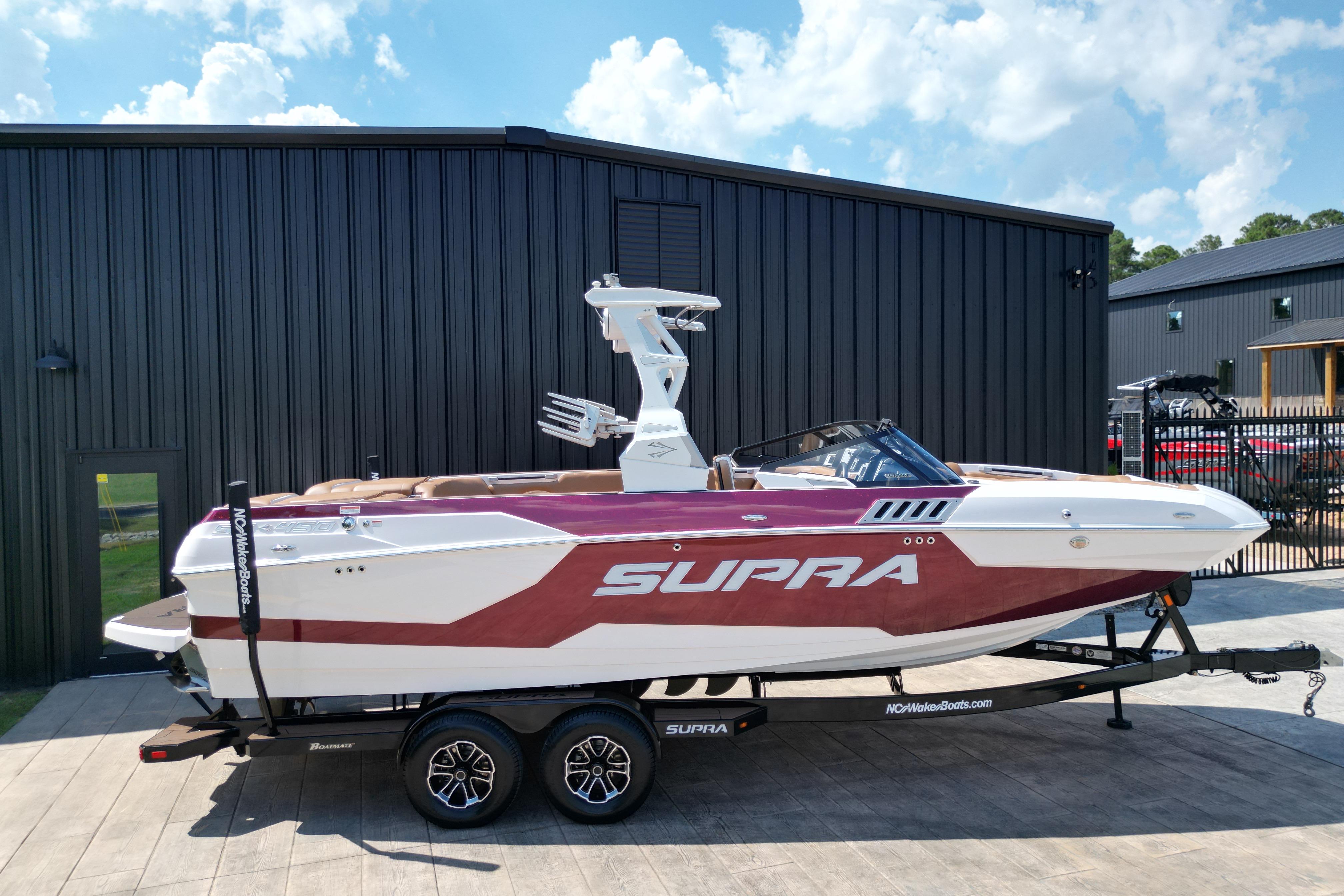 2021 Supra SE boat on trailer, parked outside a modern building under a blue sky.