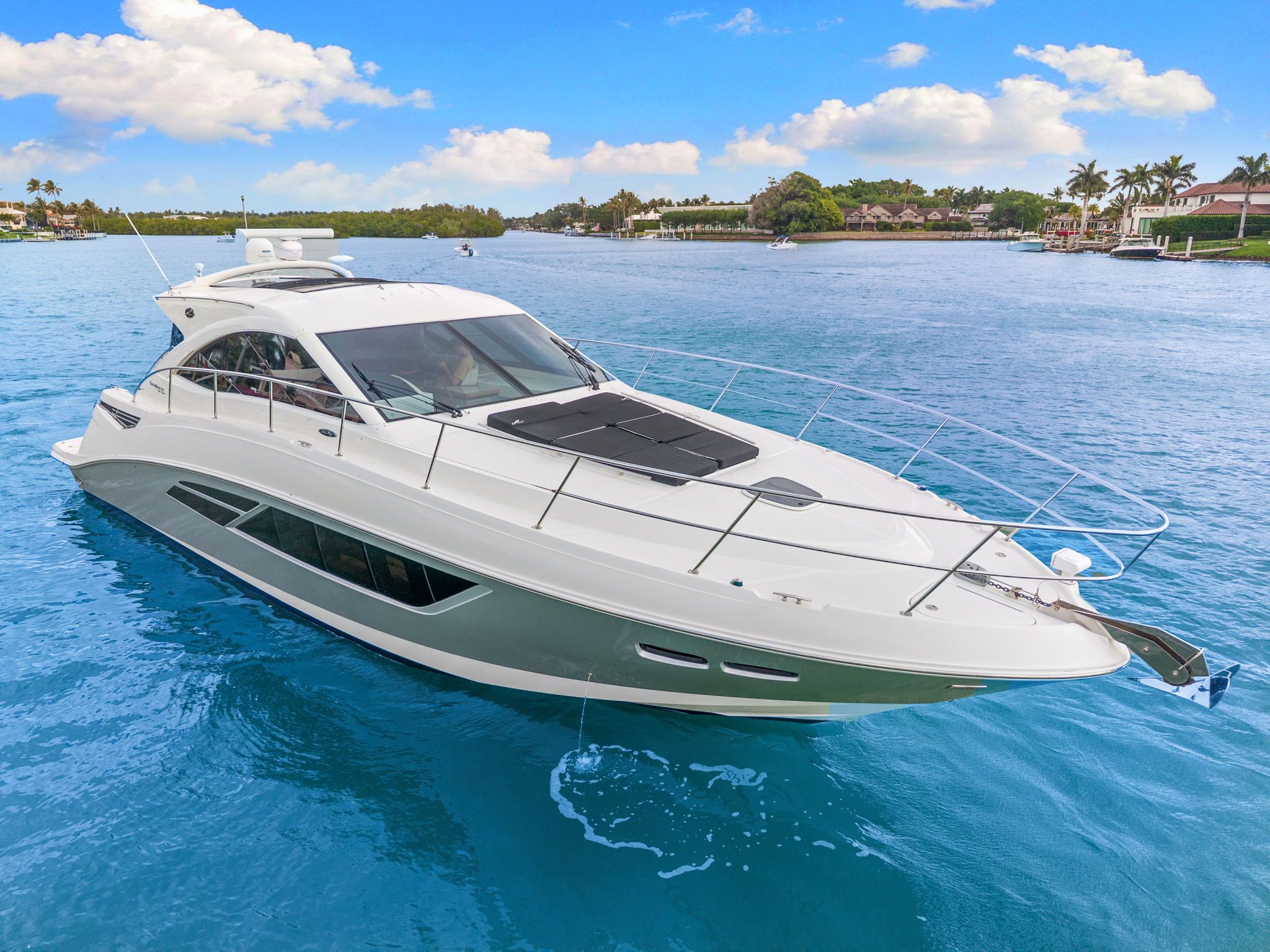 A sleek white boat cruising on calm blue water, surrounded by lush greenery.