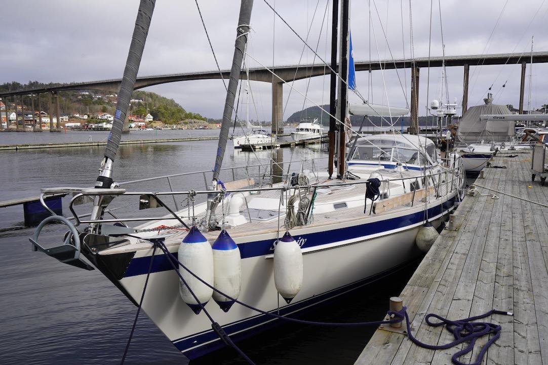 Sailboat Hallberg-Rassy 62, 2001 model, docked at a marina with scenic bridge view.