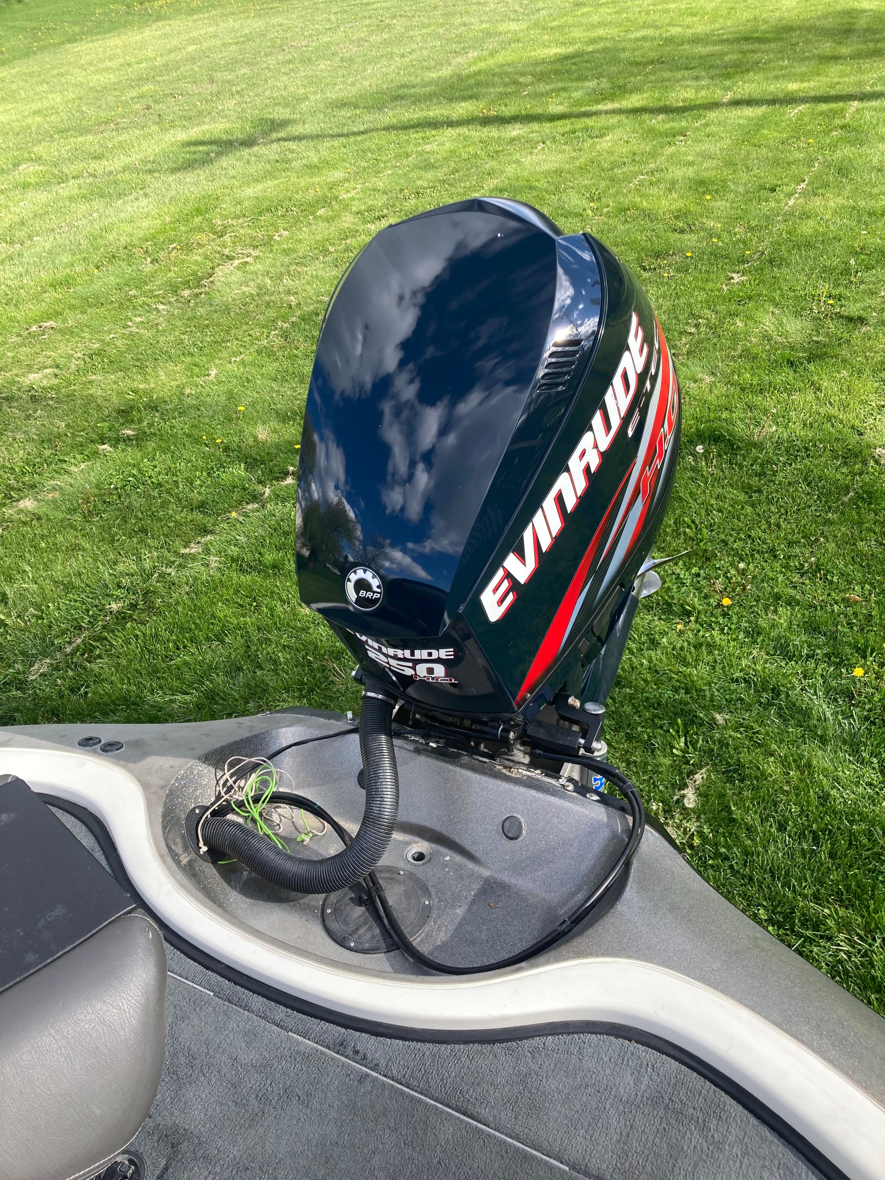 An Evinrude outboard motor is mounted on a boat situated on a grassy area.