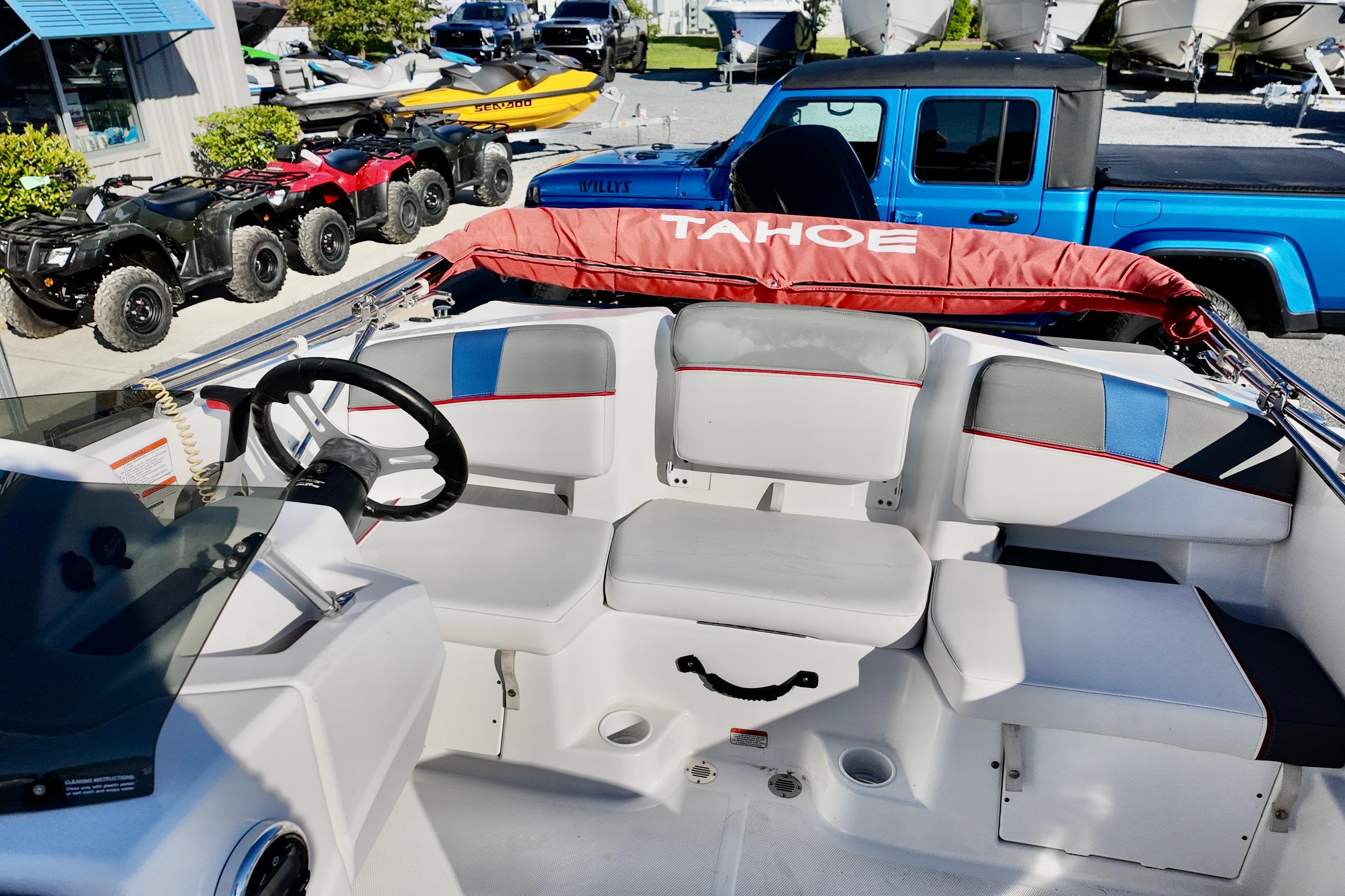 2024 Tahoe T18 boat interior with steering wheel and seating, parked near ATVs and a blue truck.