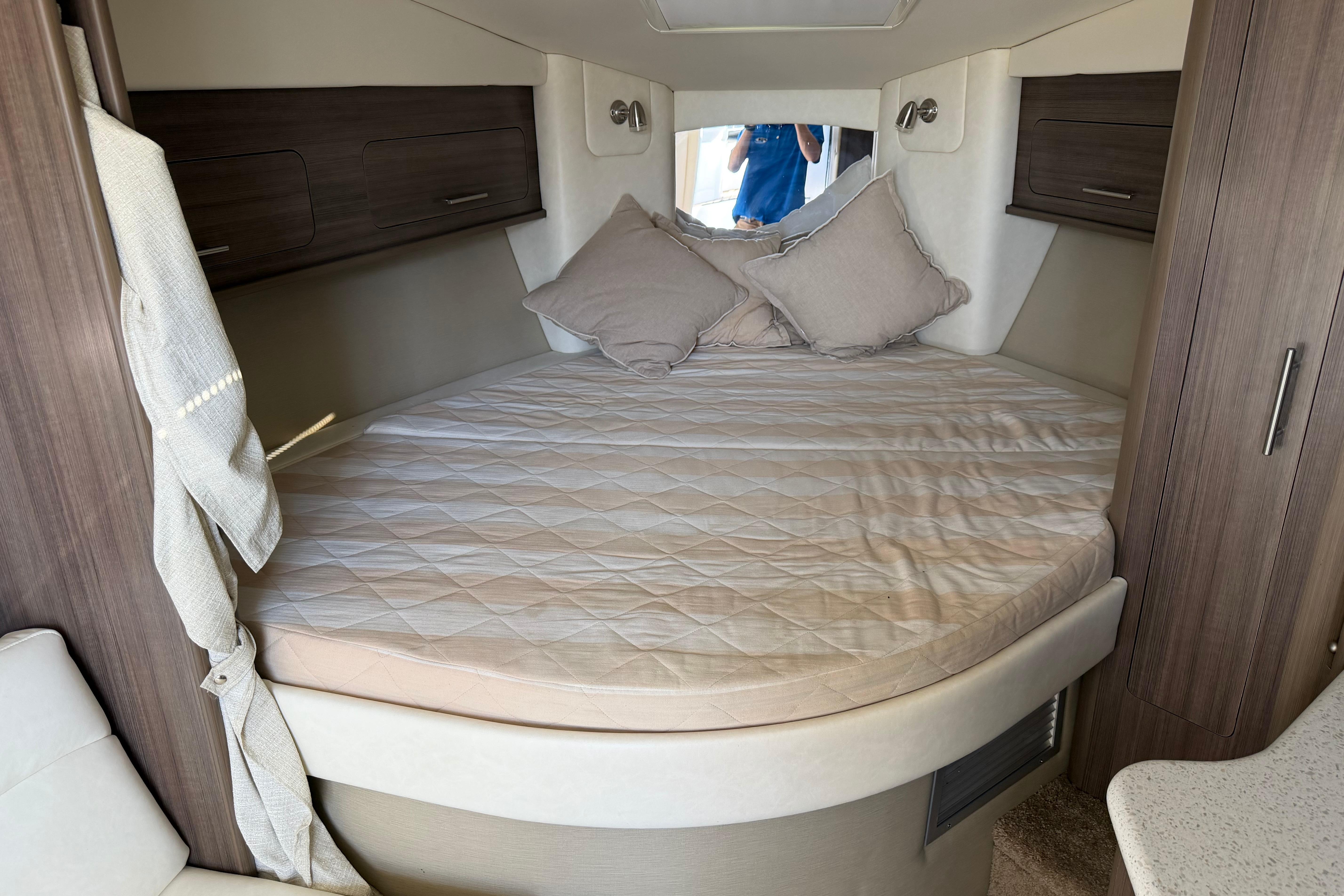 2019 Rinker EX 320 cabin interior with cozy bed and modern wood cabinetry.