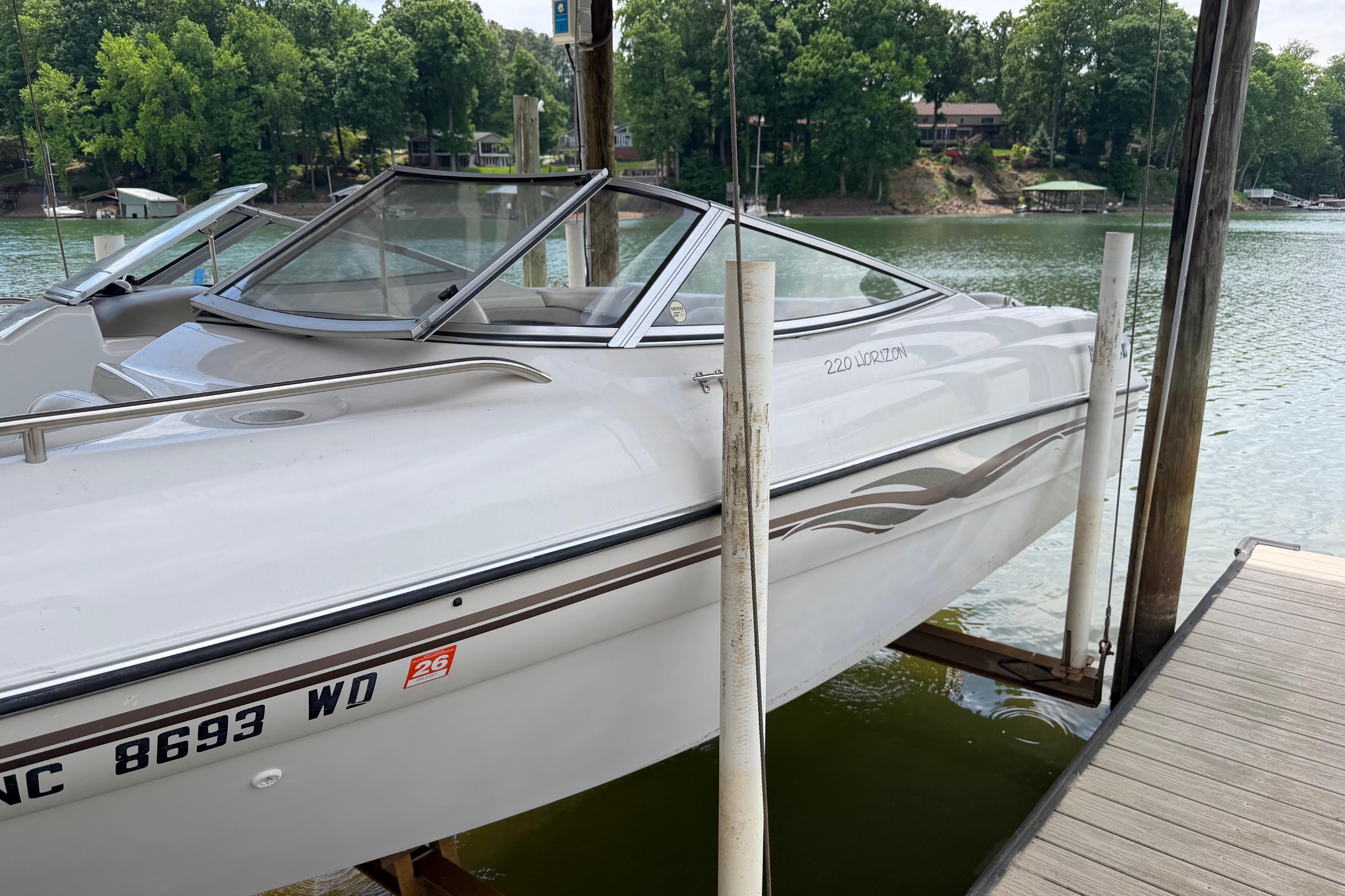 1998 Four Winns 220 Horizon boat docked on a serene lake with lush greenery.