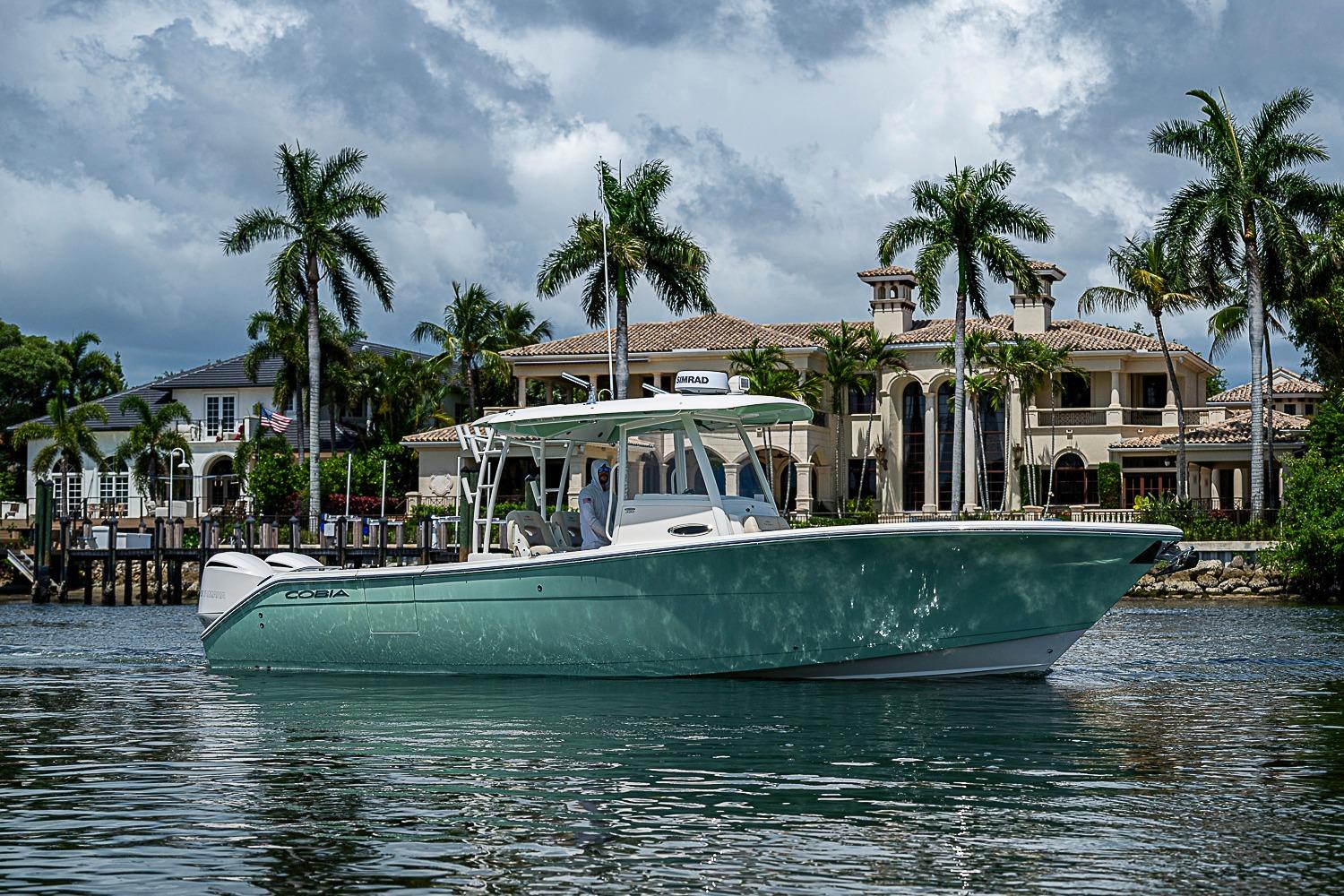 2019 Cobia 320 Center Console boat on water, luxury waterfront homes in background.