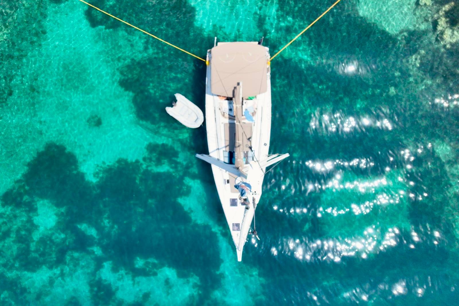 Aerial view of 2017 Dufour 512 GL yacht anchored in clear turquoise water.