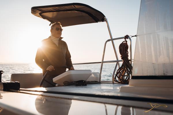 Person steering 2025 Nautitech 44 Open catamaran at sunset, with sunlit ocean backdrop.