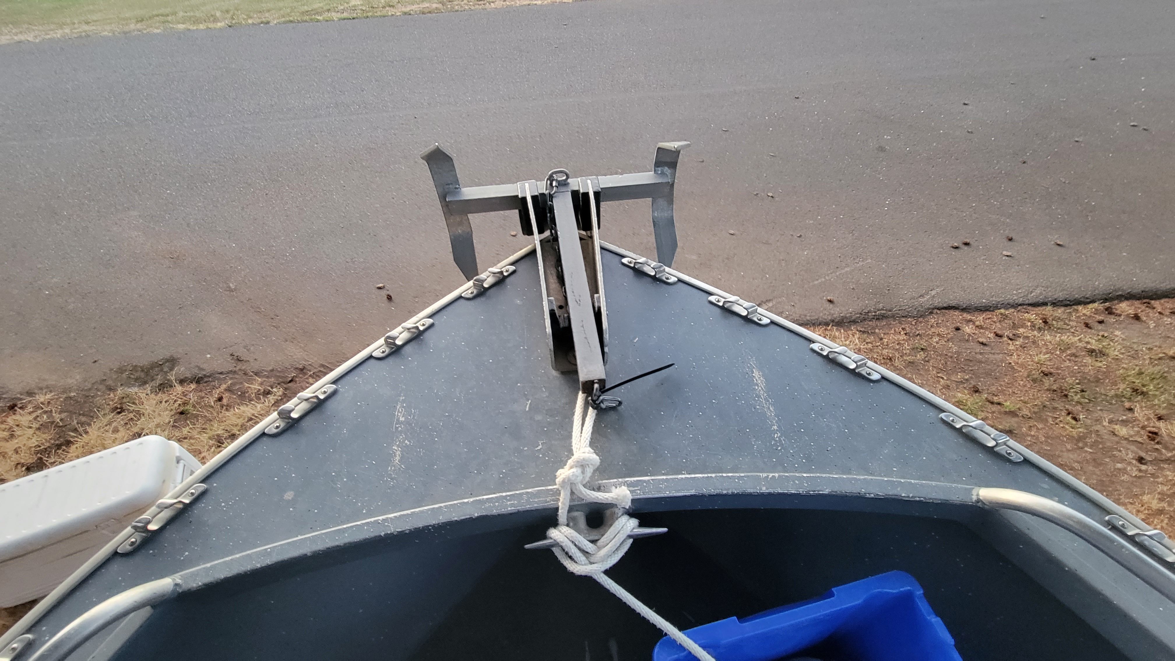 Bow of an Alumaweld boat with anchor and rope, parked on dry ground.