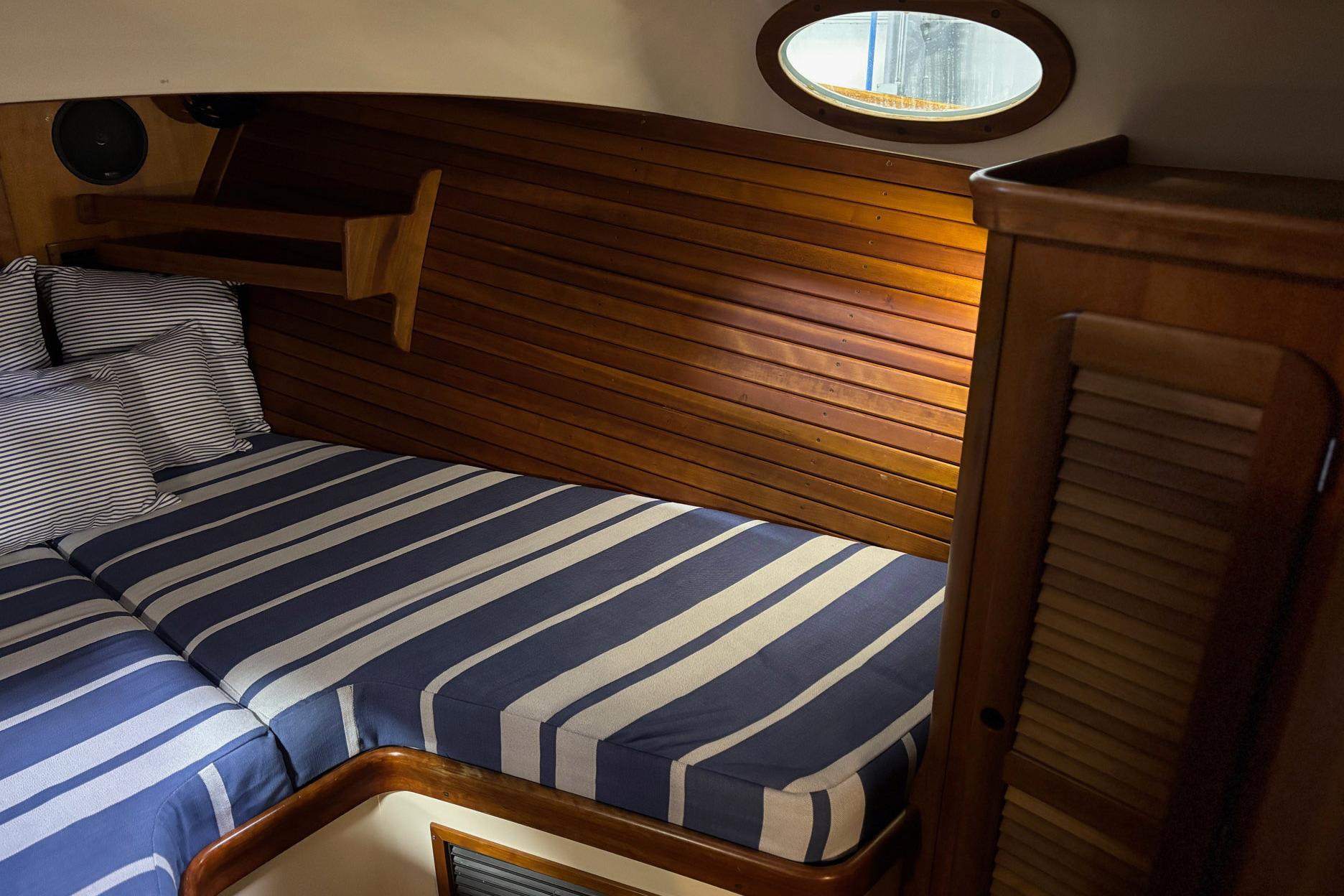 Cozy cabin interior of 2003 Hinckley 36 Picnic Boat EP with striped bedding and wooden paneling.