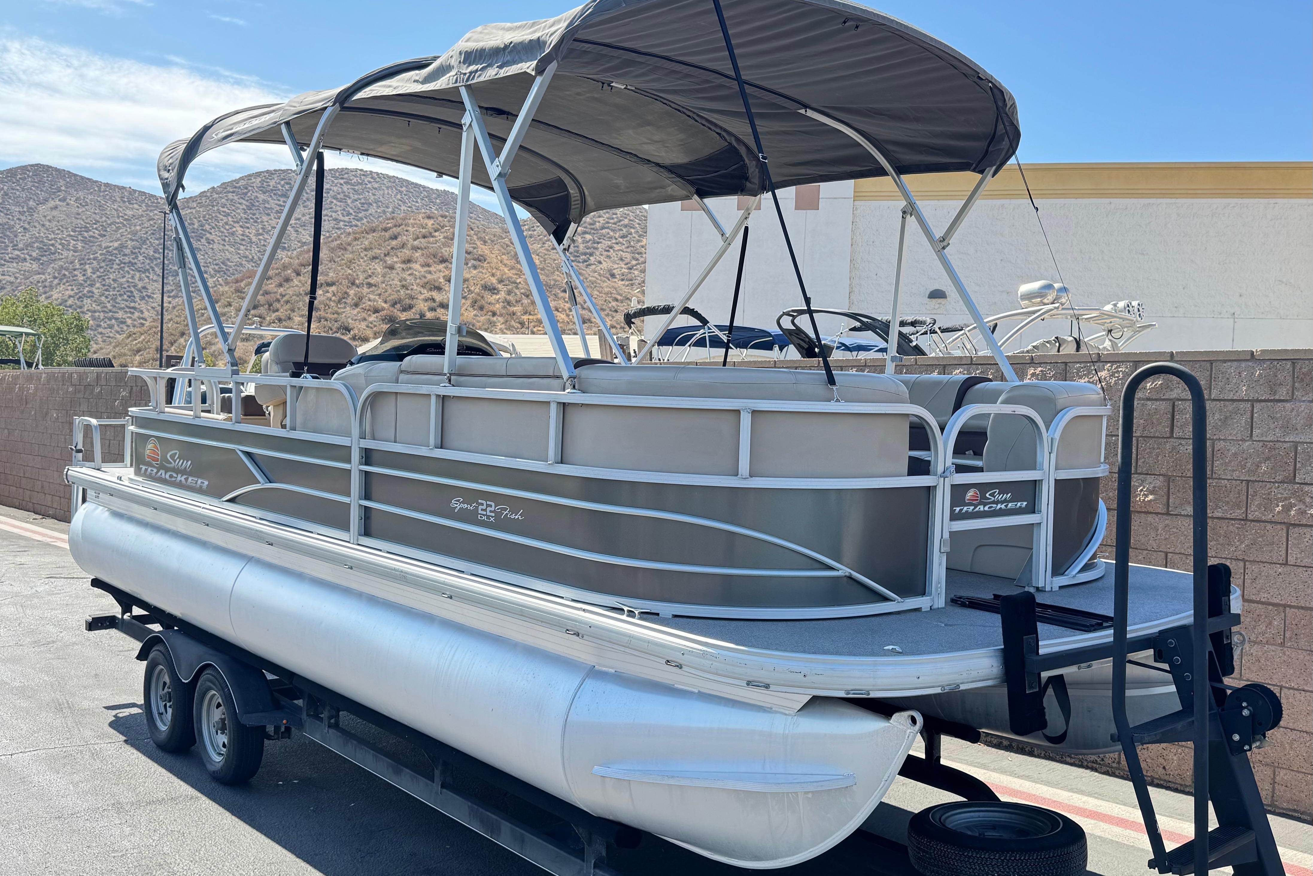 2018 Sun Tracker SportFish 22 DLX pontoon boat on trailer, parked outdoors.