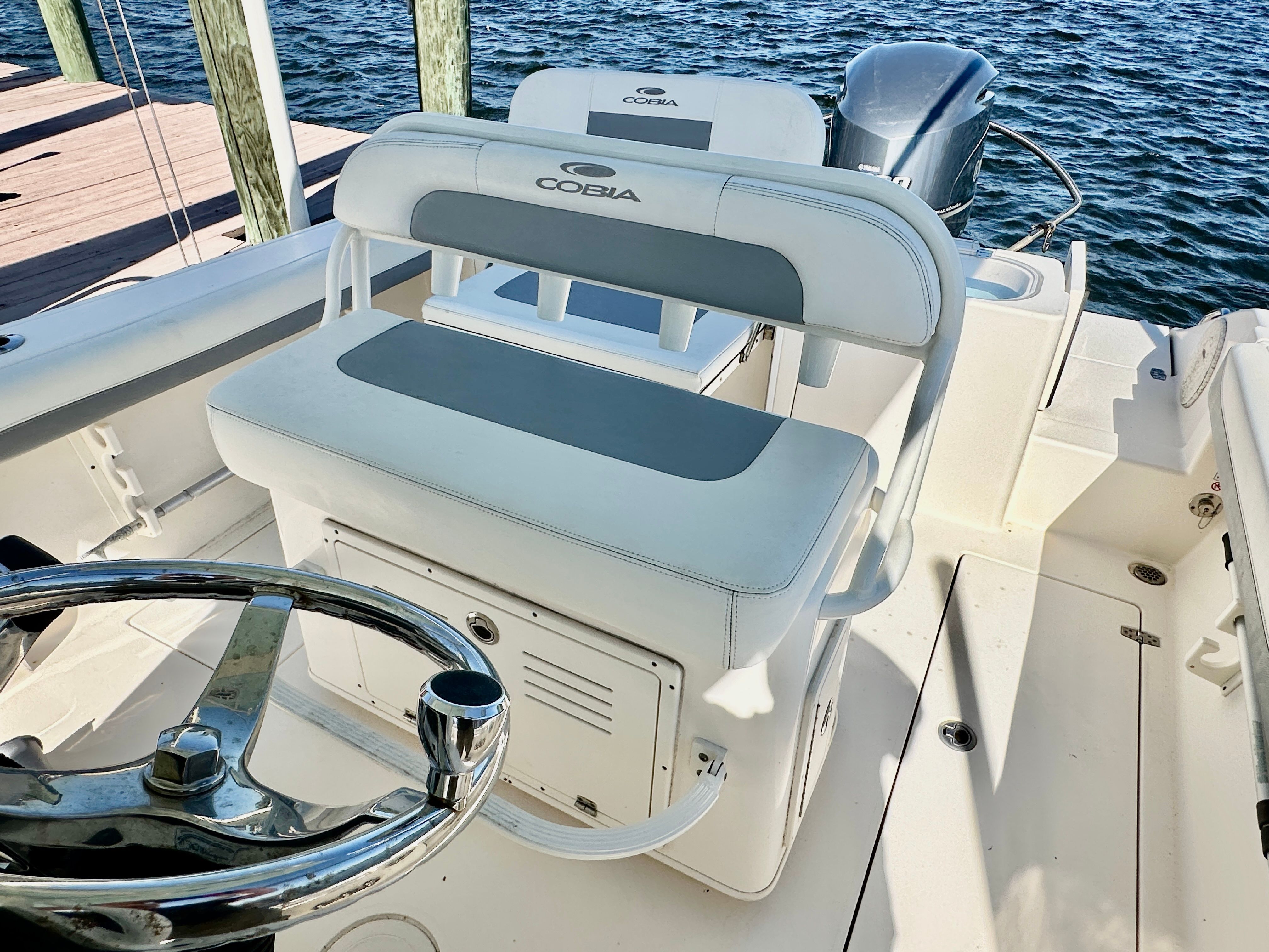 The image shows the cockpit of a 2022 Cobia 240 Center Console boat with white and gray seating.