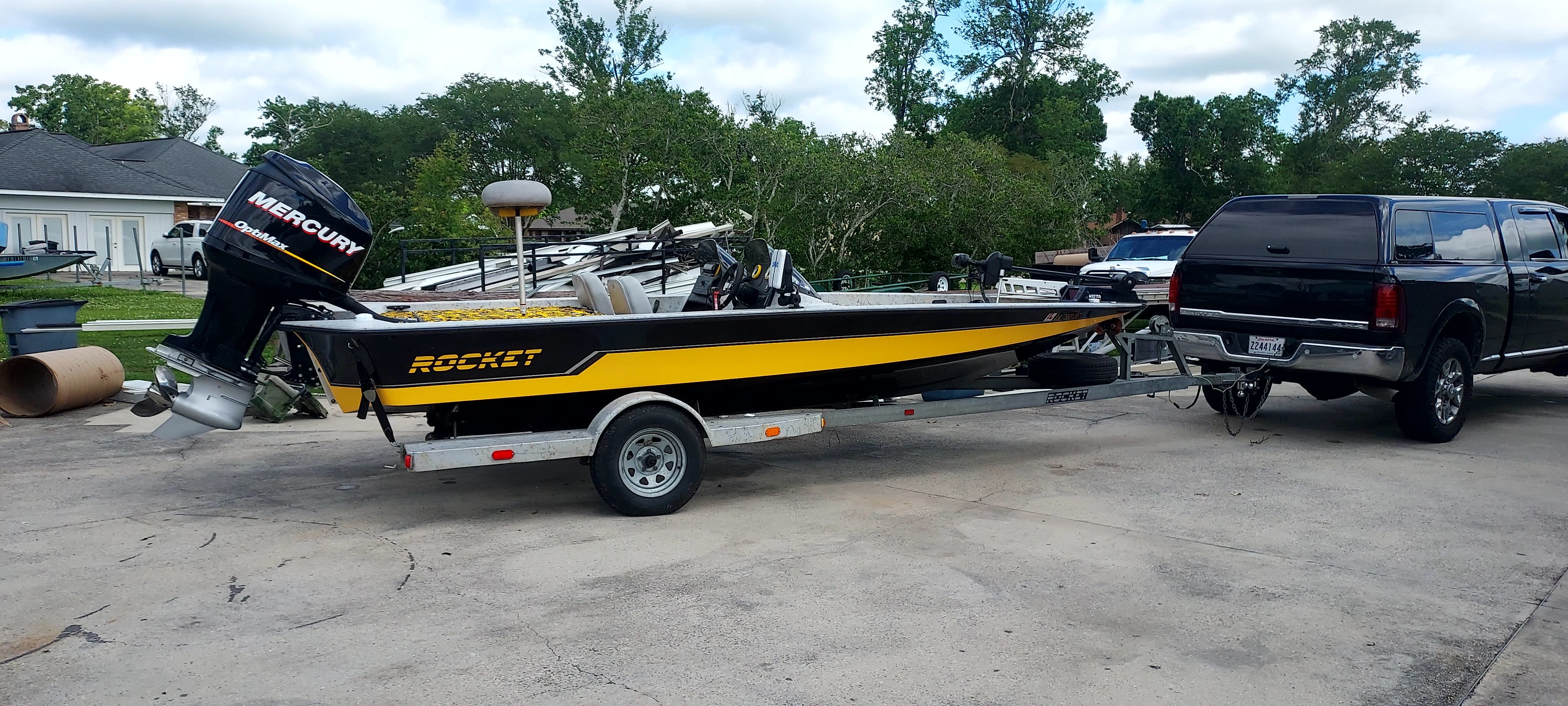 A yellow boat with a Mercury engine on a trailer, towed by a black truck.