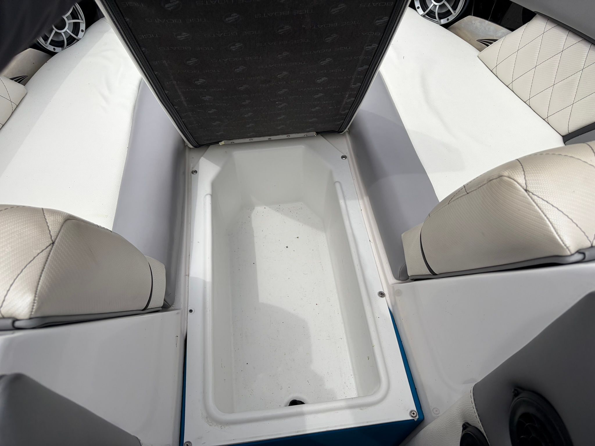 An open storage compartment on a boat with white upholstery and a black lid.