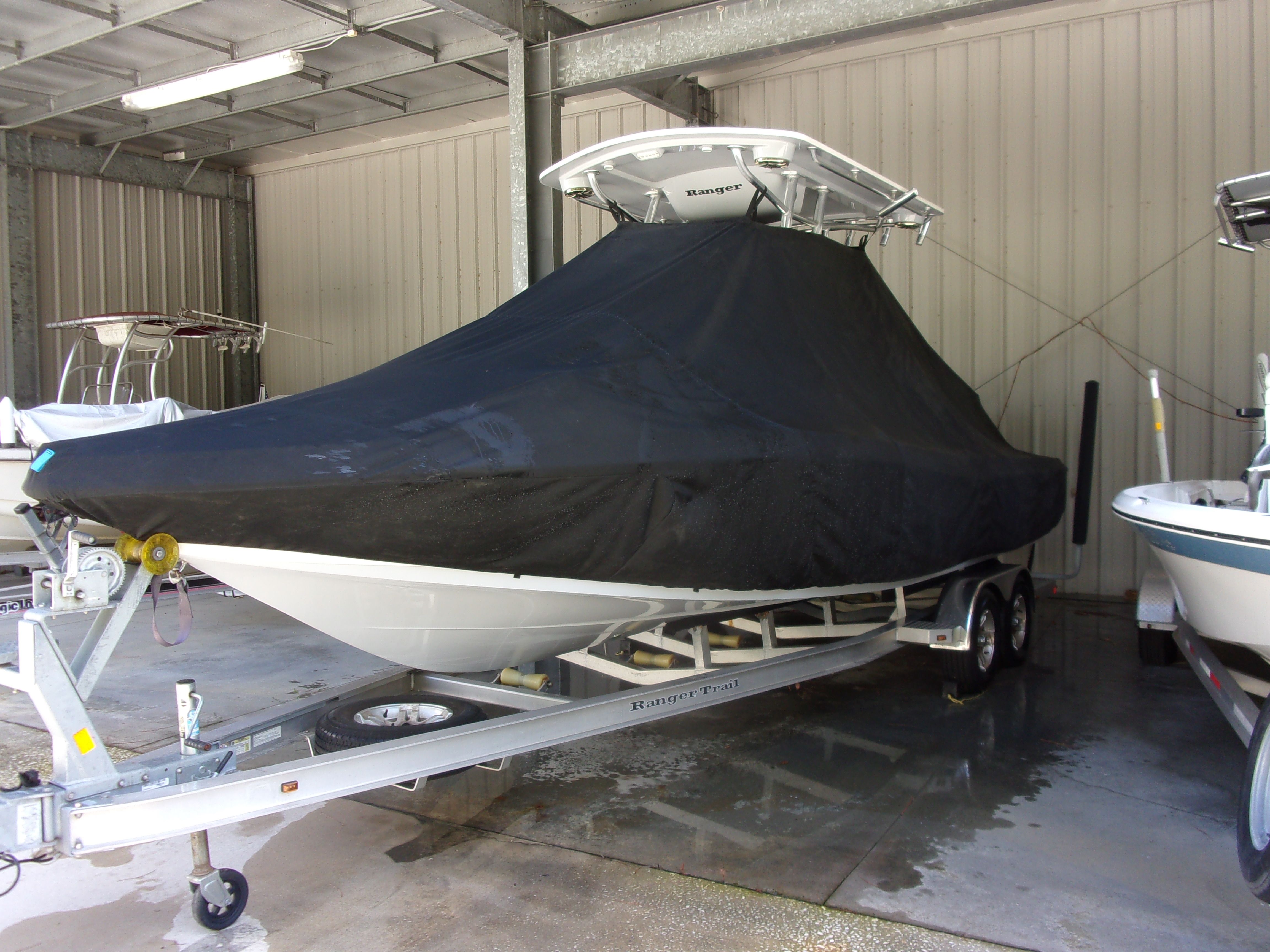 A 2019 Ranger 2510 Bay Ranger boat is covered with a black cover and sits on a trailer in a sheltered area.