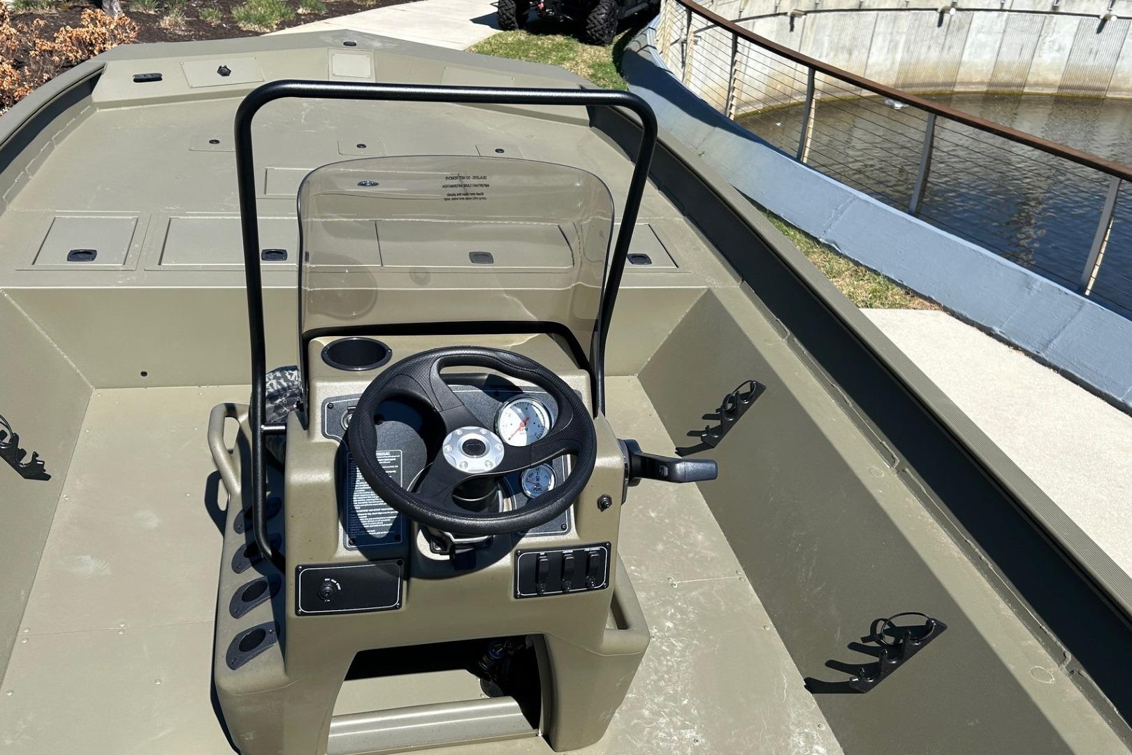 2026 Tracker Grizzly 2072 CC boat console with steering wheel and controls, docked by a waterway.