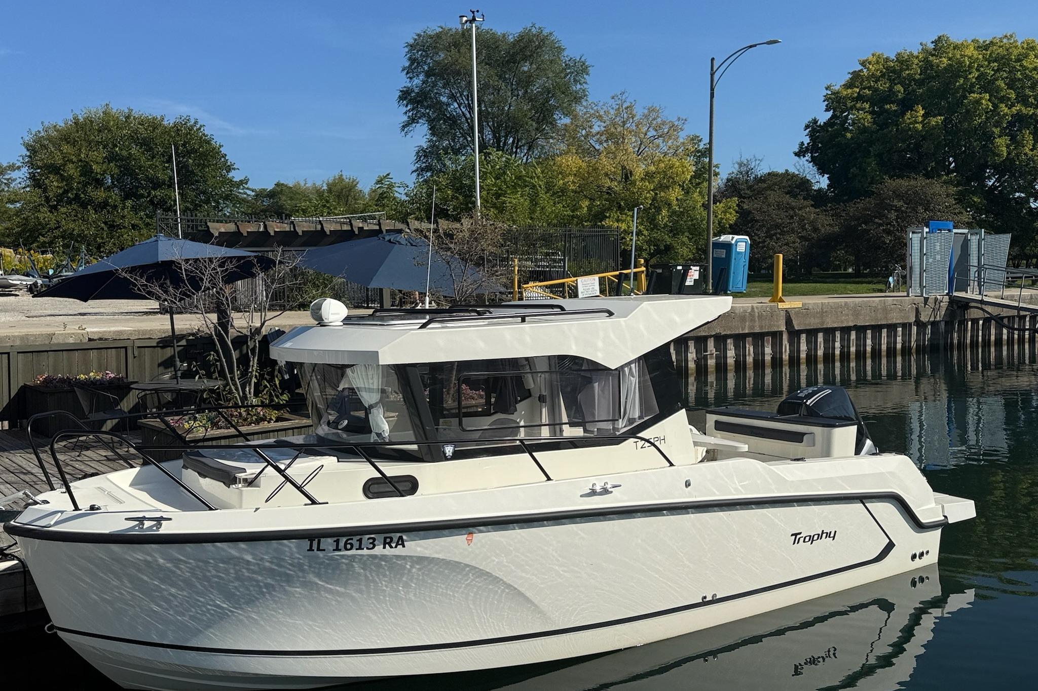 2024 Bayliner Trophy T25 Pilothouse boat docked by a scenic waterfront.