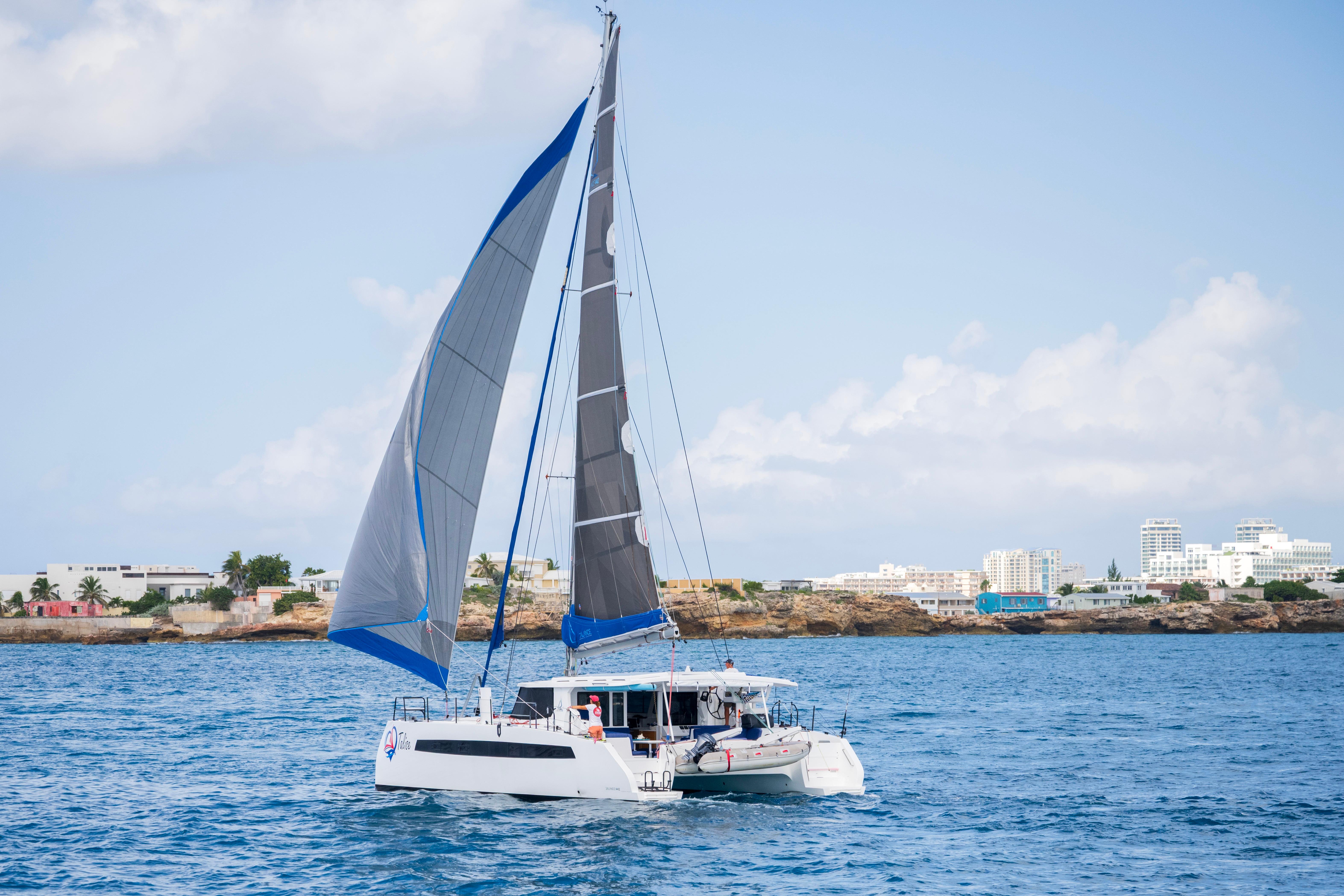 2024 Balance 442 catamaran sailing near a coastal city under a clear blue sky.