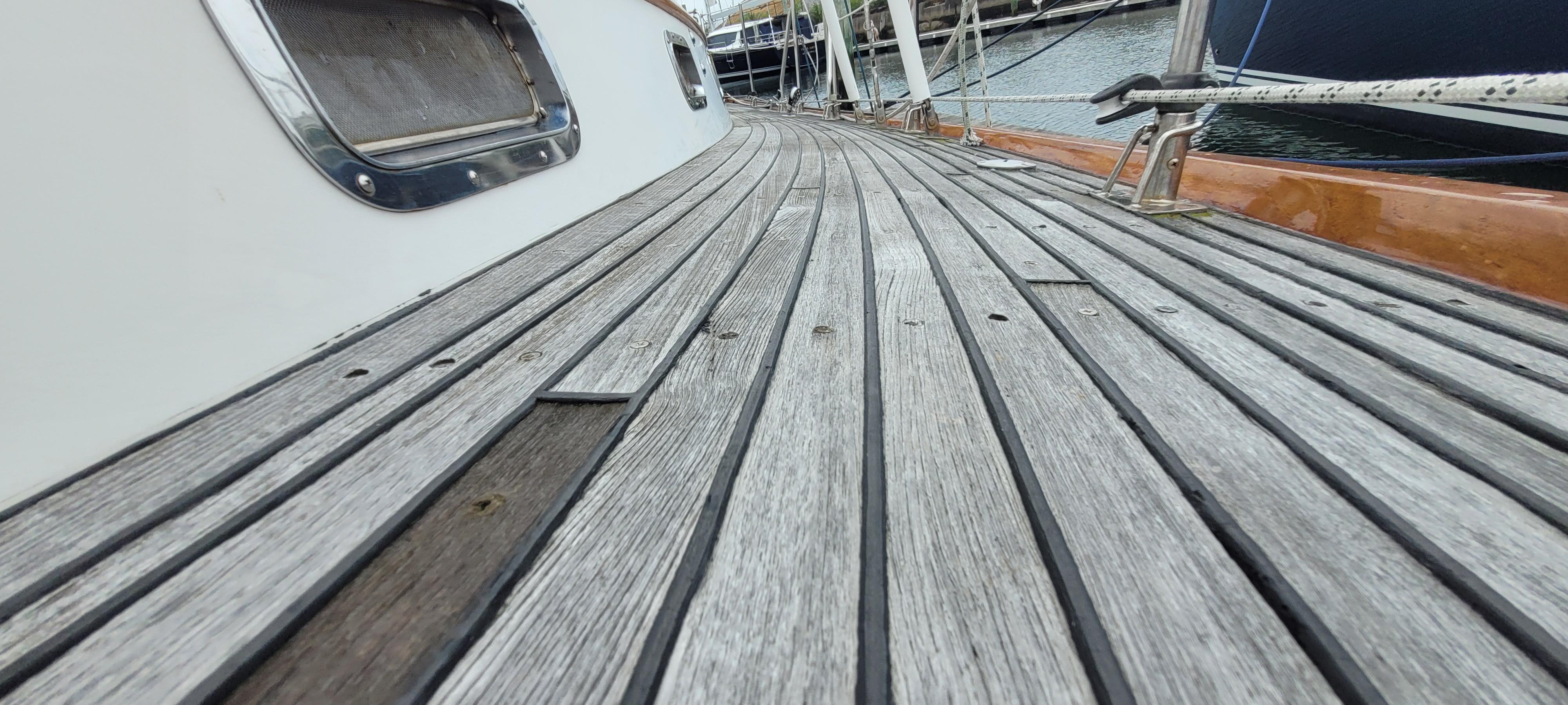 Deck of 1985 Mason 33 Sloop with wooden planks and metal fittings, docked at marina.