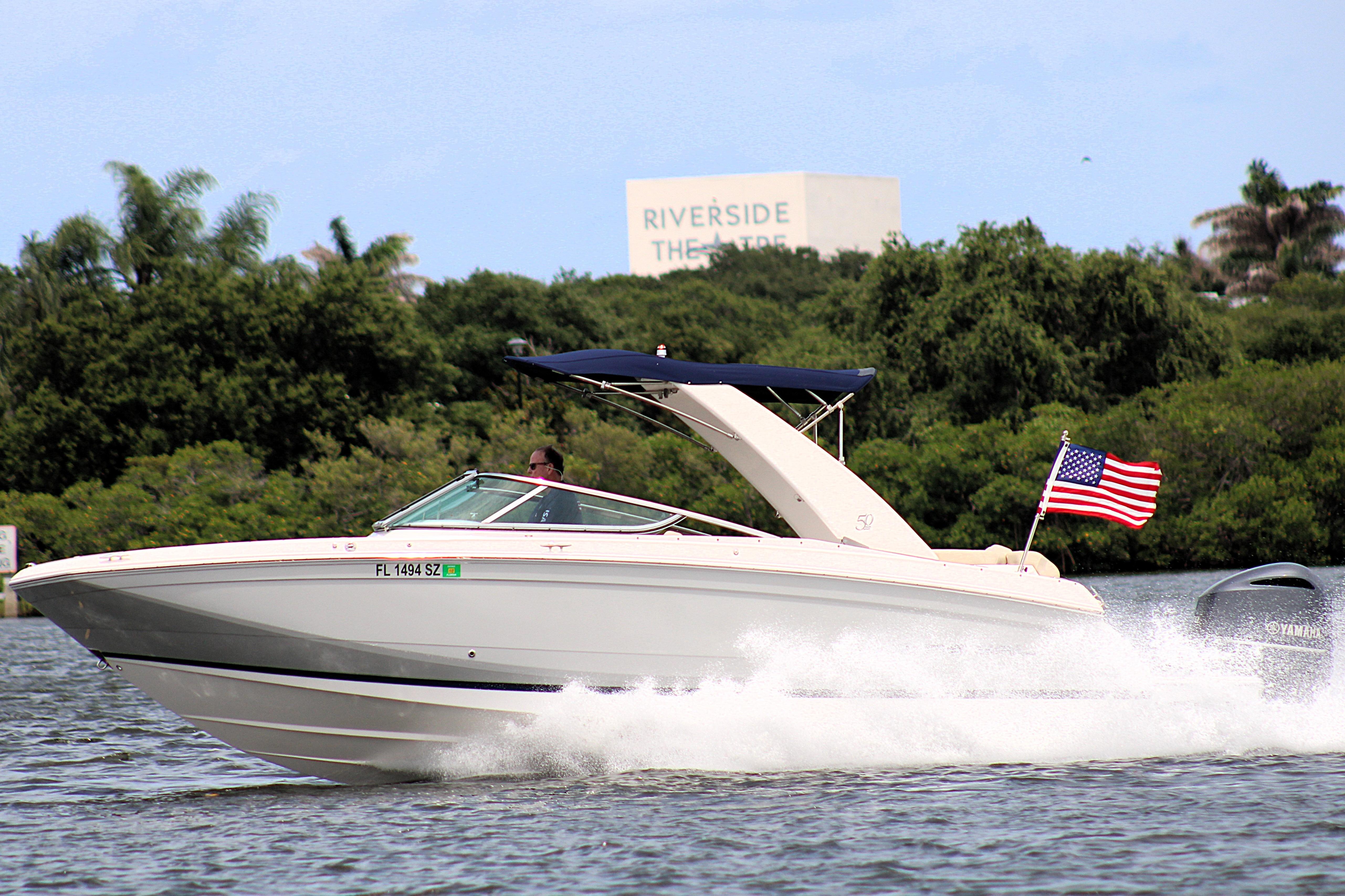 2021 Regal 26 OBX boat cruising on water with American flag, lush greenery background.