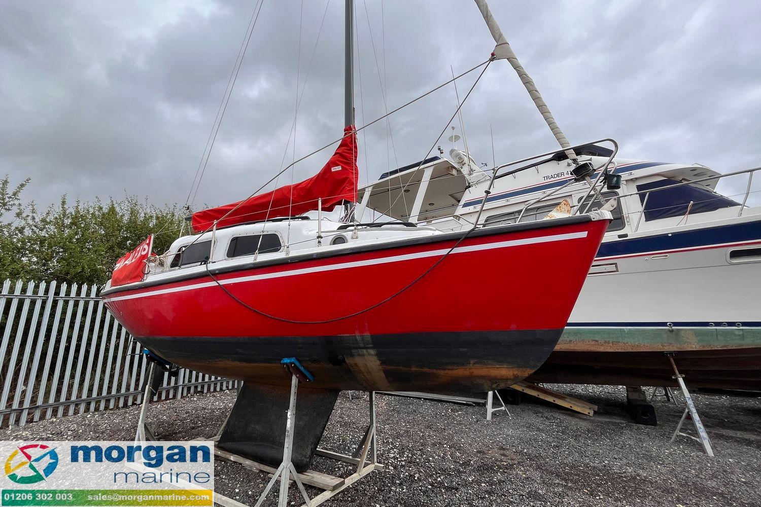 Red 1979 Leisure 23 sailboat on display at Morgan Marine, overcast sky background.