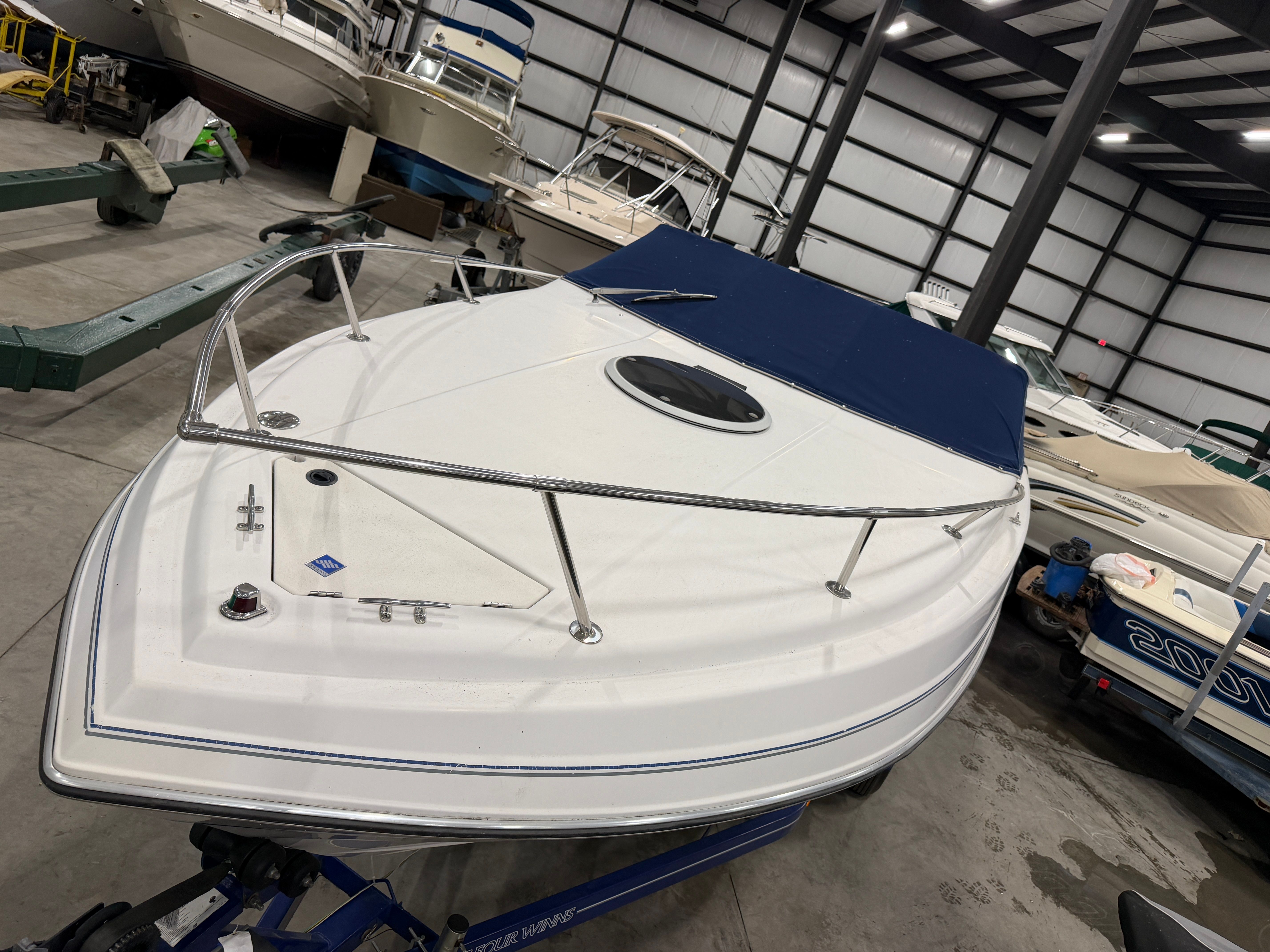 A 1992 Four Winns 225 Sundowner in a storage facility, featuring a blue cover and stainless steel railing.